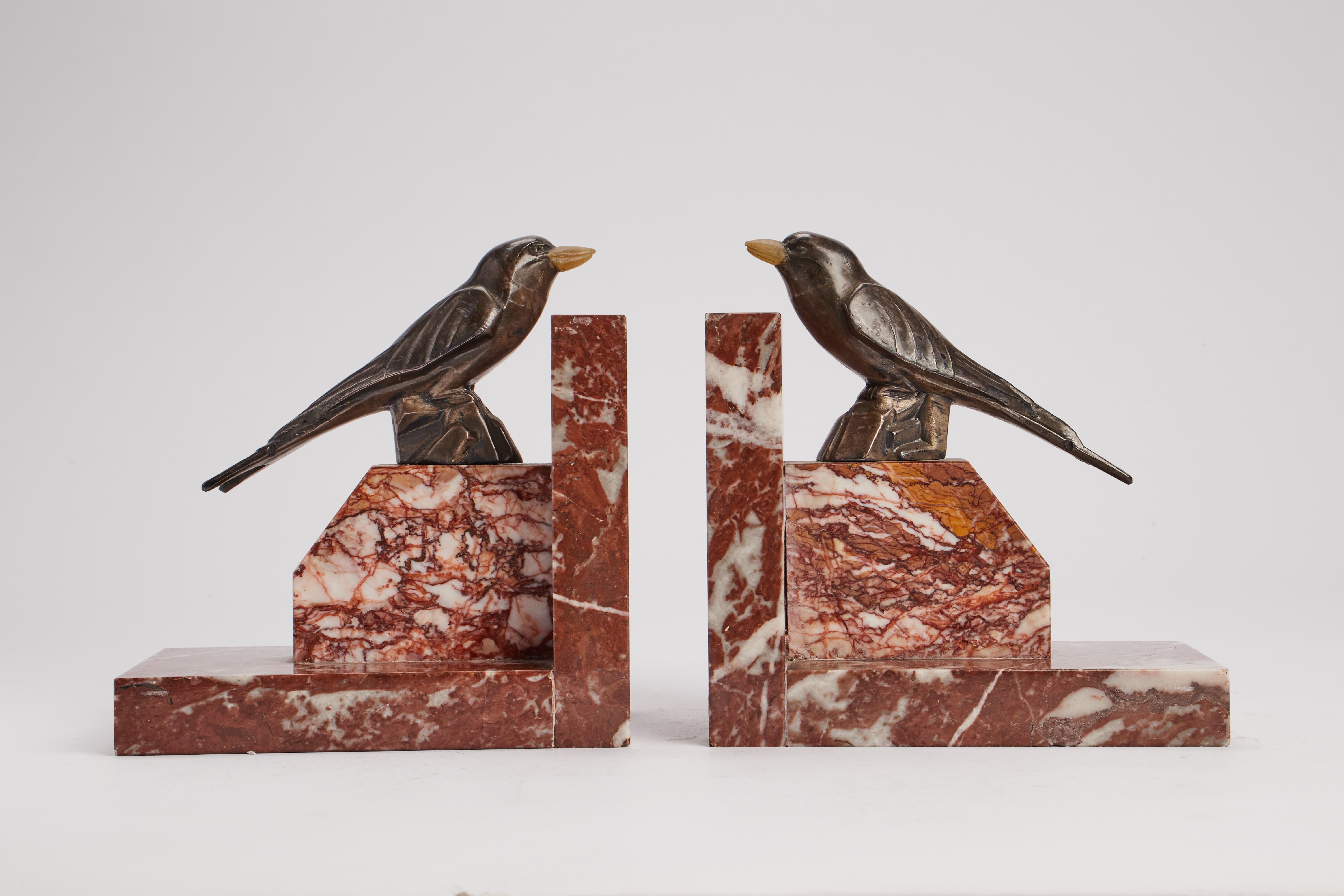 Coppia di reggilibri in marmo rosso venato di Verona con struttura ortogonale a forma di L. Sulla base in marmo sono presenti due sculture identiche in metallo bianco, raffiguranti due uccelli Whiting. Il becco è fatto di corno. Art Deco, Francia,