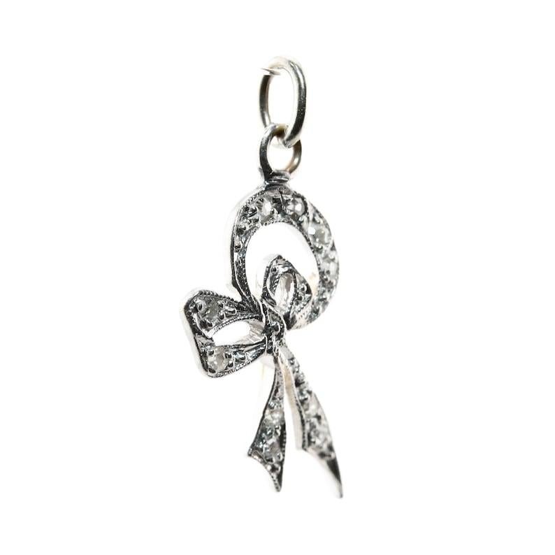 Aston Estate Jewelry Presents:

An Art Deco period diamond set ribbon style charm in the shape of a bow. Set throughout with ten diamonds of 0.25ctw with H color and SI clarity. Accented by miligrain beading and engraved detailing.

Tested as