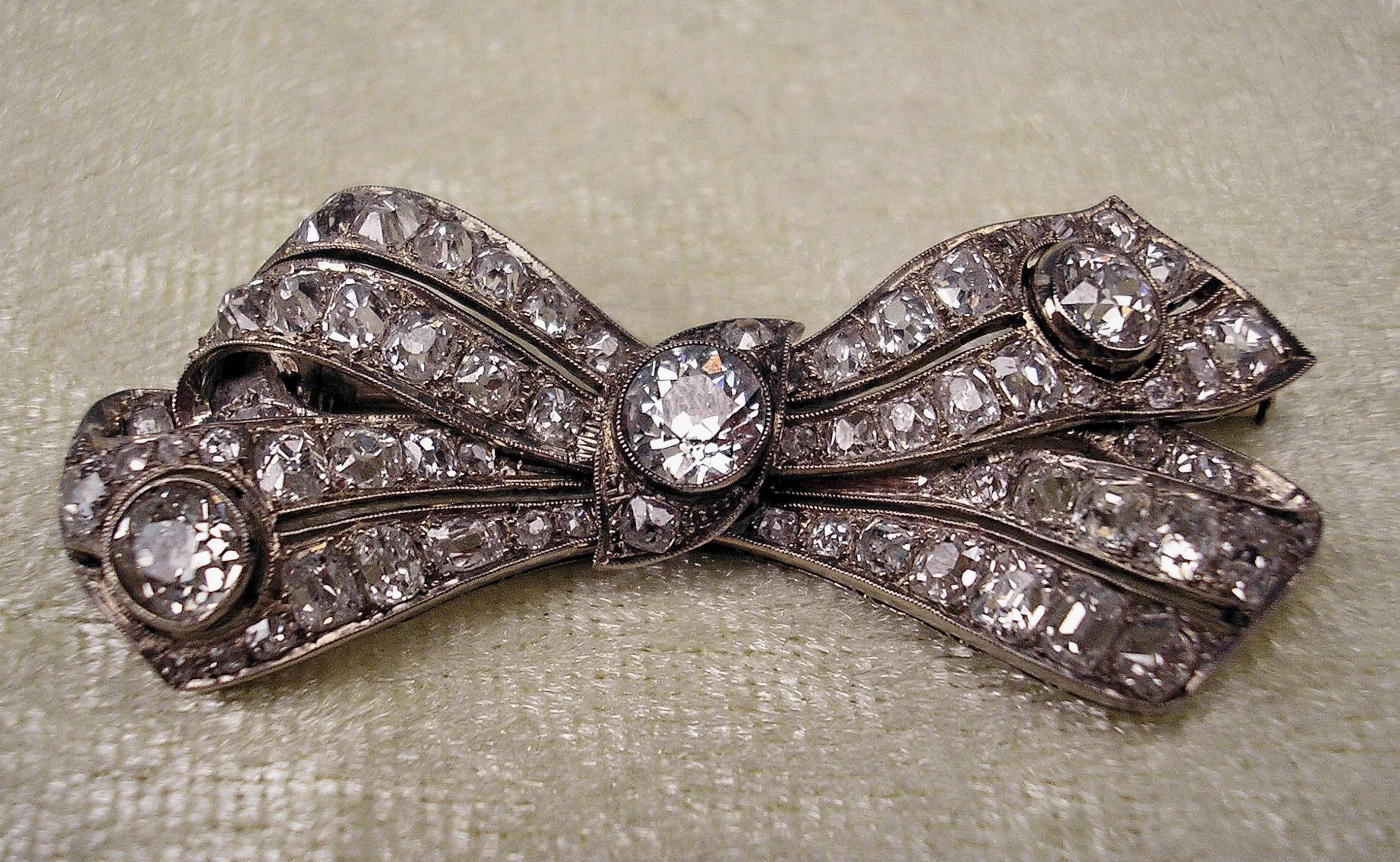 Finest Art Déco jewelry piece:
Bow mesh shaped brooch abundantly covered with small old European cut diamonds and three larger stones set in a diagonal, ca. 5.30 ct in total, safety closure existing.

14 ct / 858 white gold
Austrian official