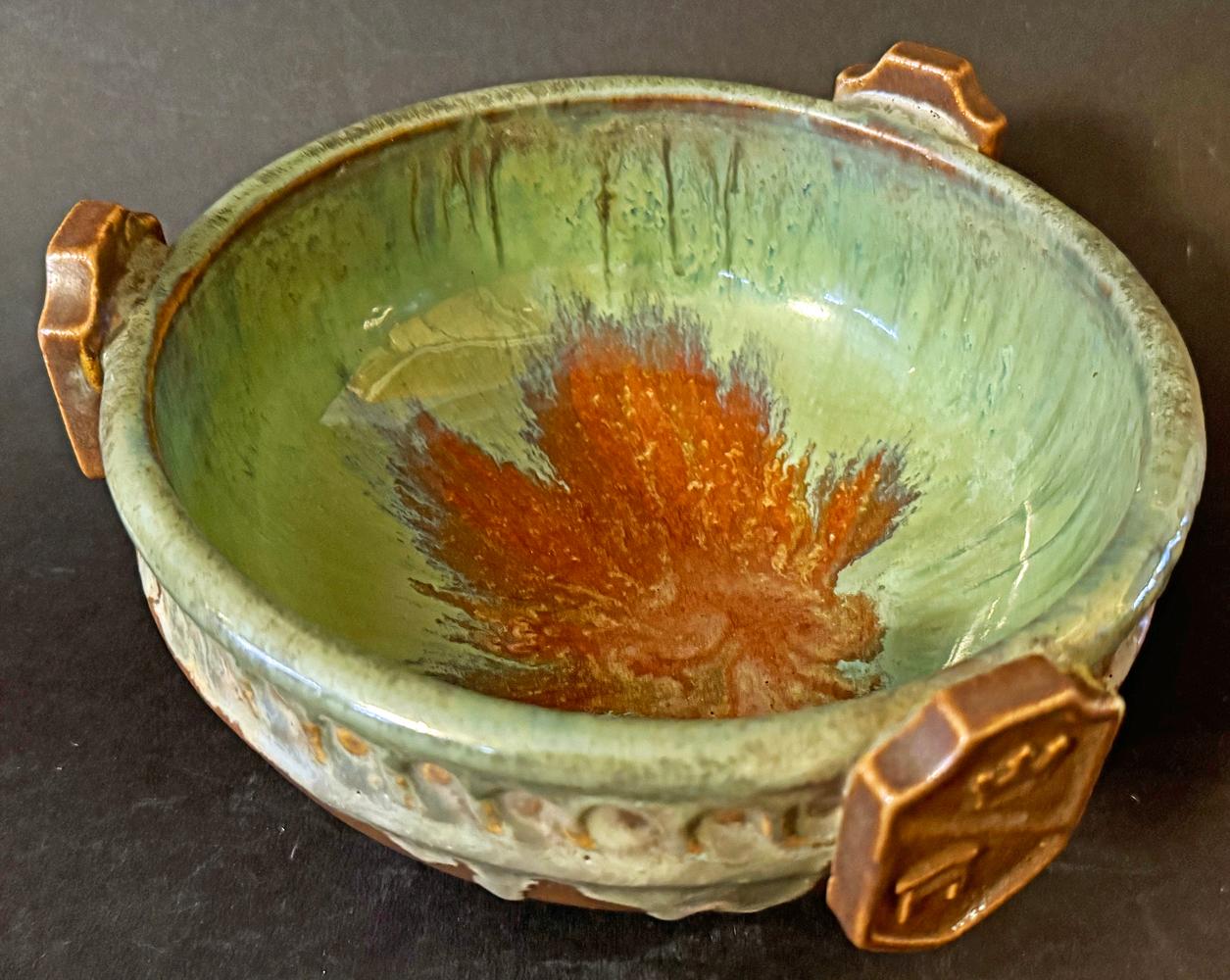 Rare et frappant, ce bol Art déco de la célèbre Fulper Pottery présente ses glaçures flambe à l'intérieur du bol - dans des tons caramel, vert et bleu - ainsi que trois boucliers d'influence médiévale appliqués sur le bord, chacun avec un casque de