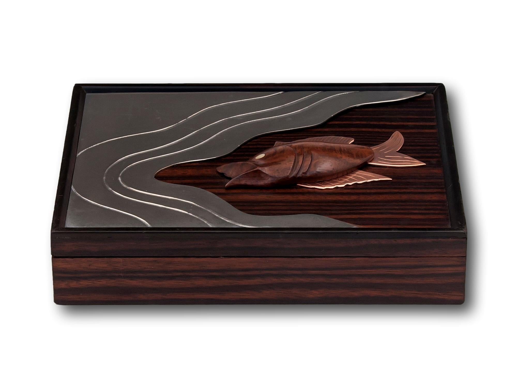 Lined in Royal Blue Padded Velvet

From our Boxes collection, we are pleased to offer this Art Deco Macassar Ebony Box. The box of slim rectangular form with an inset scene featuring a Fish with copper fins and a brass eye swimming with chrome