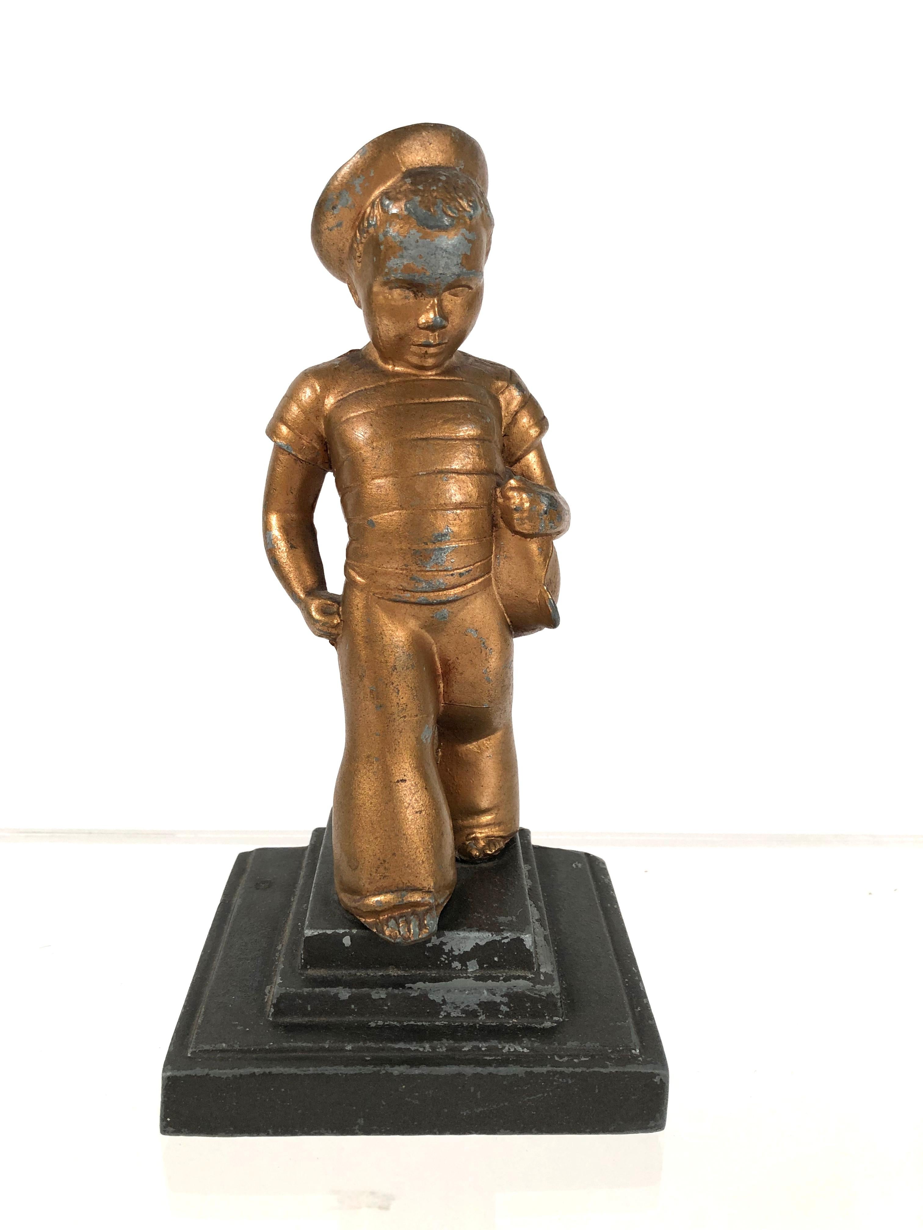 An Art Deco period gold painted cast iron figure of a little boy with striped sailor shirt, hat and pants, holding a toy sailboat, on a stepped rectangular grey painted plinth. A well modeled and expressive figure, one of a pair of bookends. Marked