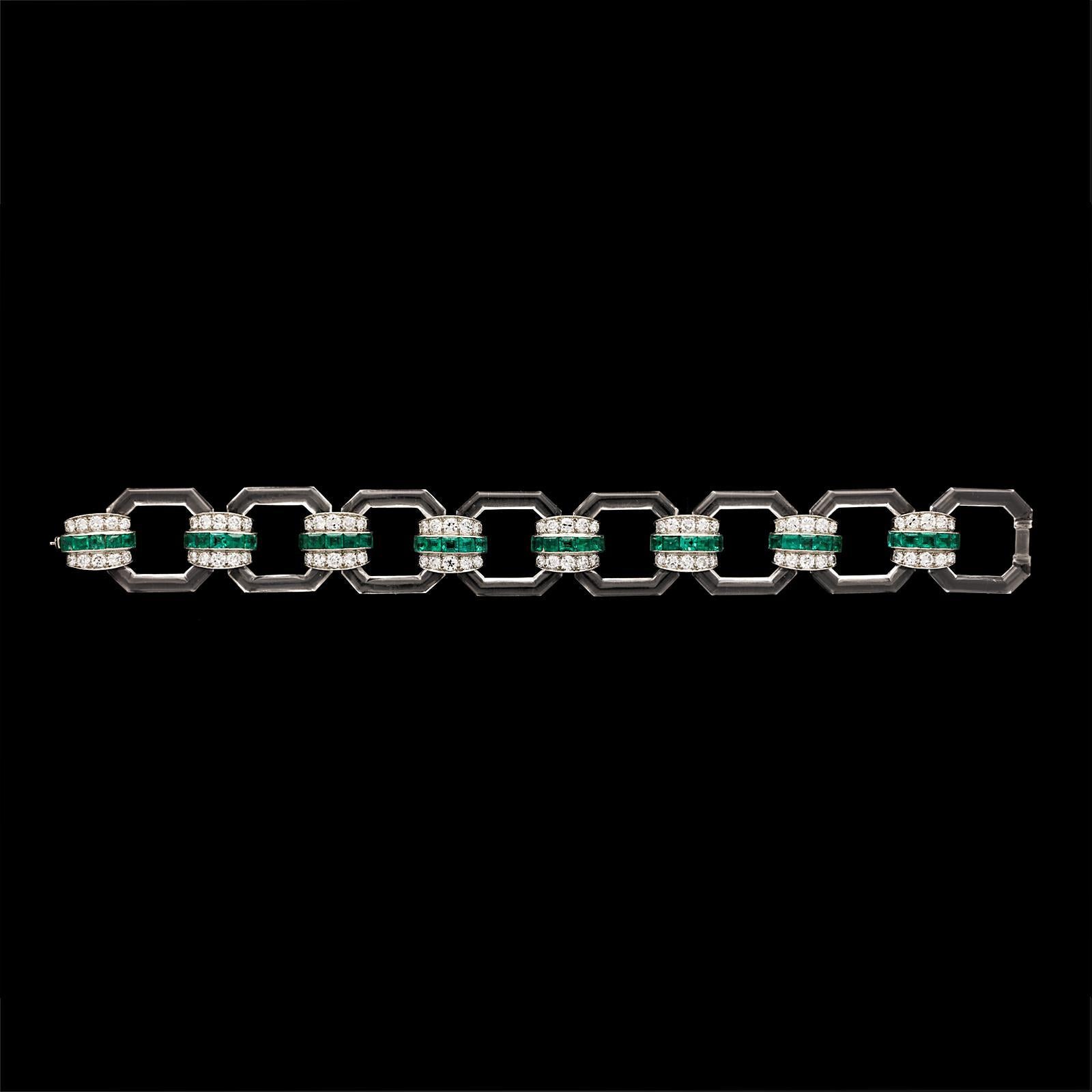 A stunning Art Deco bracelet by Hennell 1929, formed of eight open uniform octagonal links carved from colourless transparent rock crystal quartz and joined by tonneau-shaped platinum links set to the centre with a row of calibré-cut emeralds