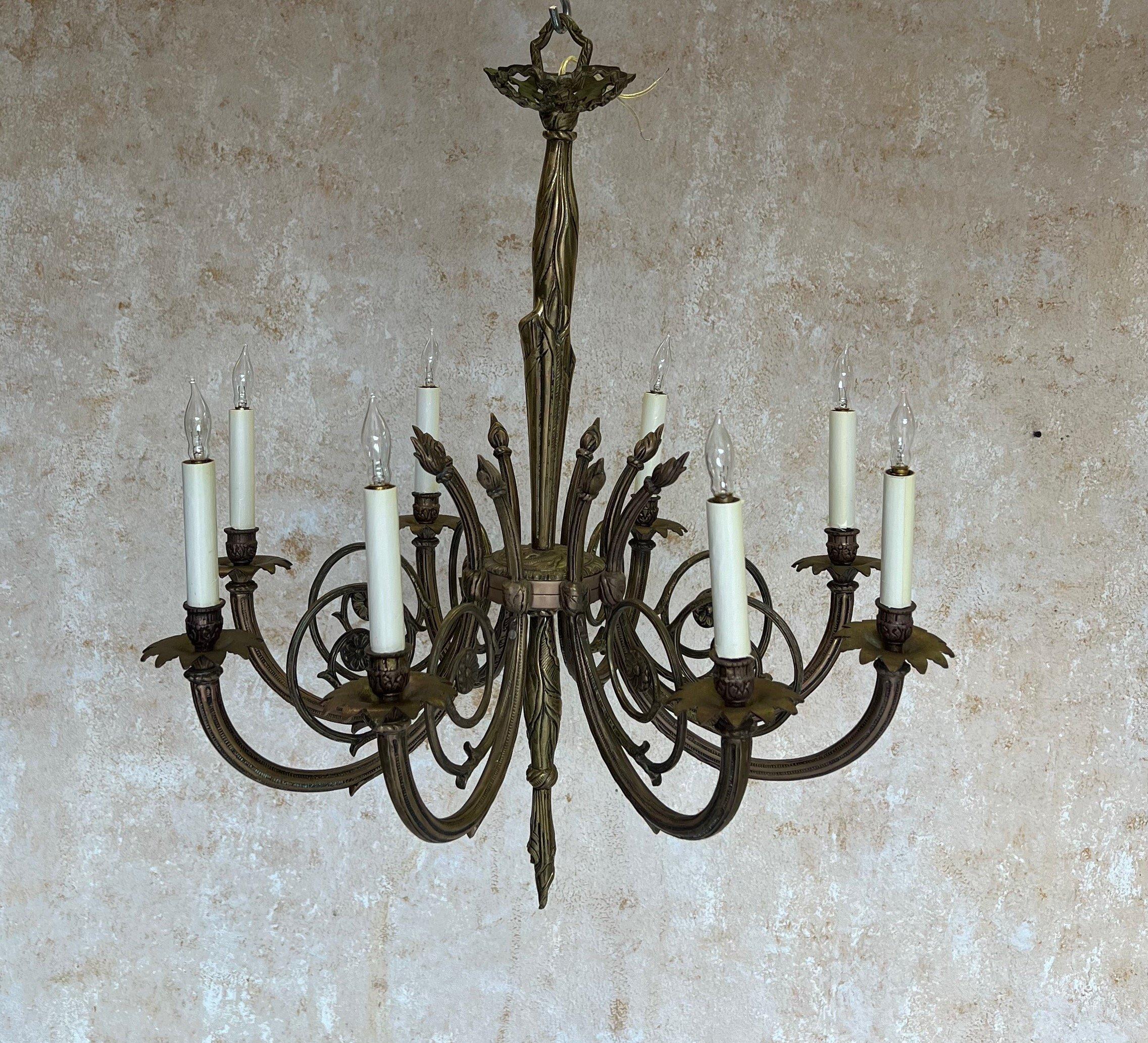 This magnificent French 1920s Art Deco chandelier is crafted from intricately detailed brass and bronze components. It features eight spiraling arms clustered around a central stem with stylized drapery adornment. In very good vintage condition, it