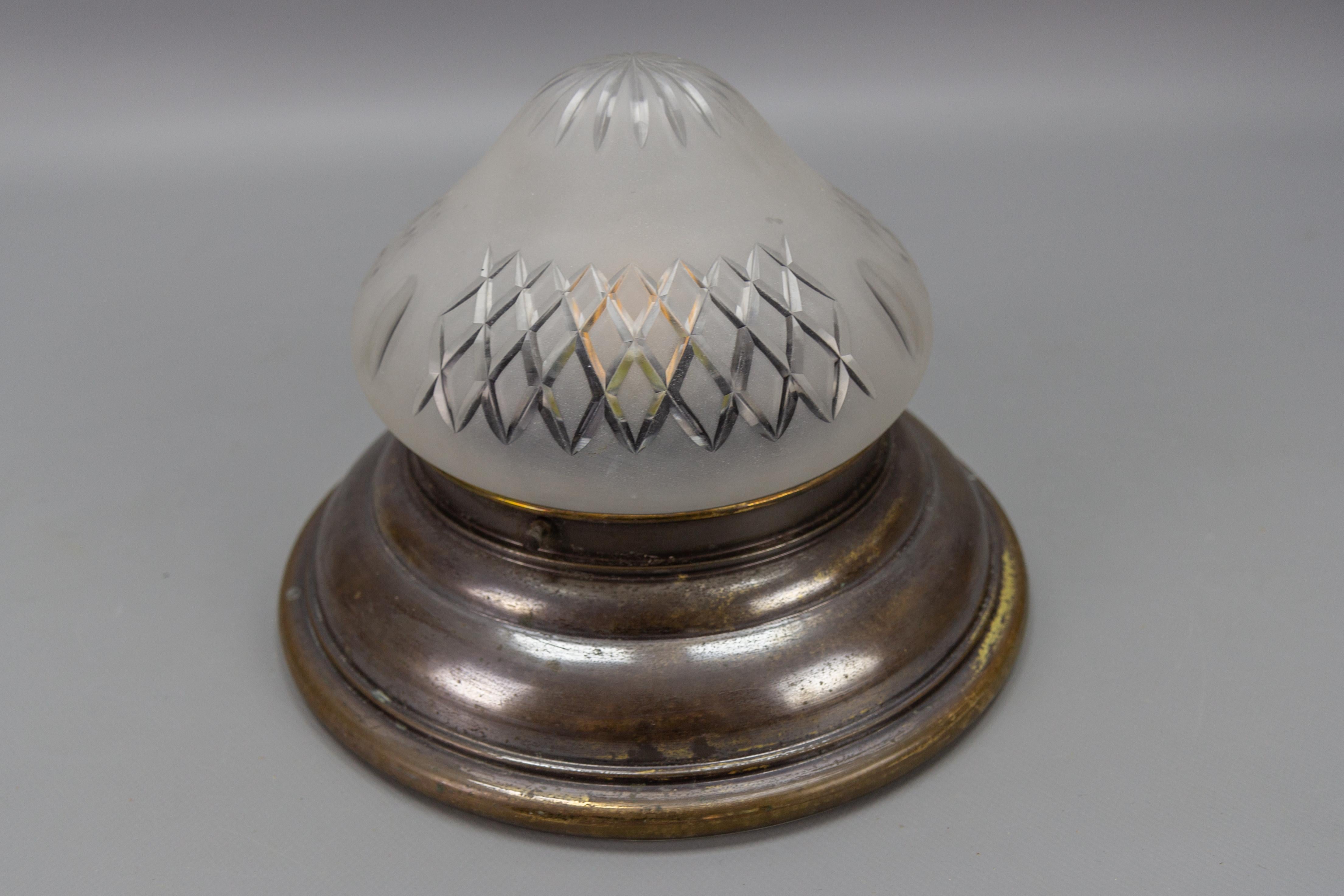 Art Deco brass and cut white frosted glass flush mount, circa 1930.
This classic and elegant ceiling light fixture features a round brass frame with a beautifully shaped white frosted glass lamp shade with cut ornaments. 
Dimensions: height: 17.5 cm
