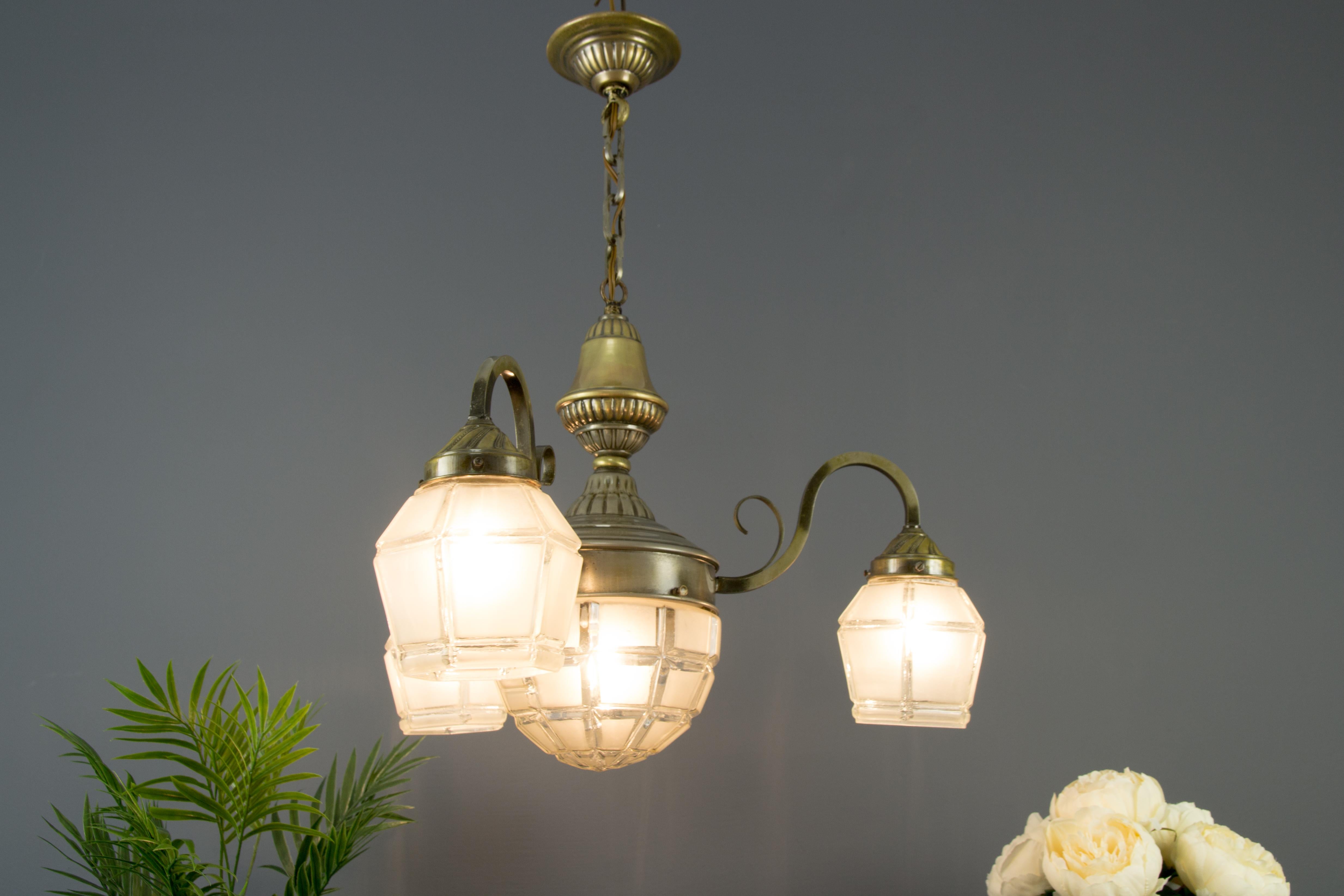 An elegant French Art Deco chandelier from the 1930s. Three brass arms, each with a white frosted glass shade, and one socket for the E 27 light bulb. The bottom is centered with a frosted glass bowl and one socket for the E 27-size (E26) light