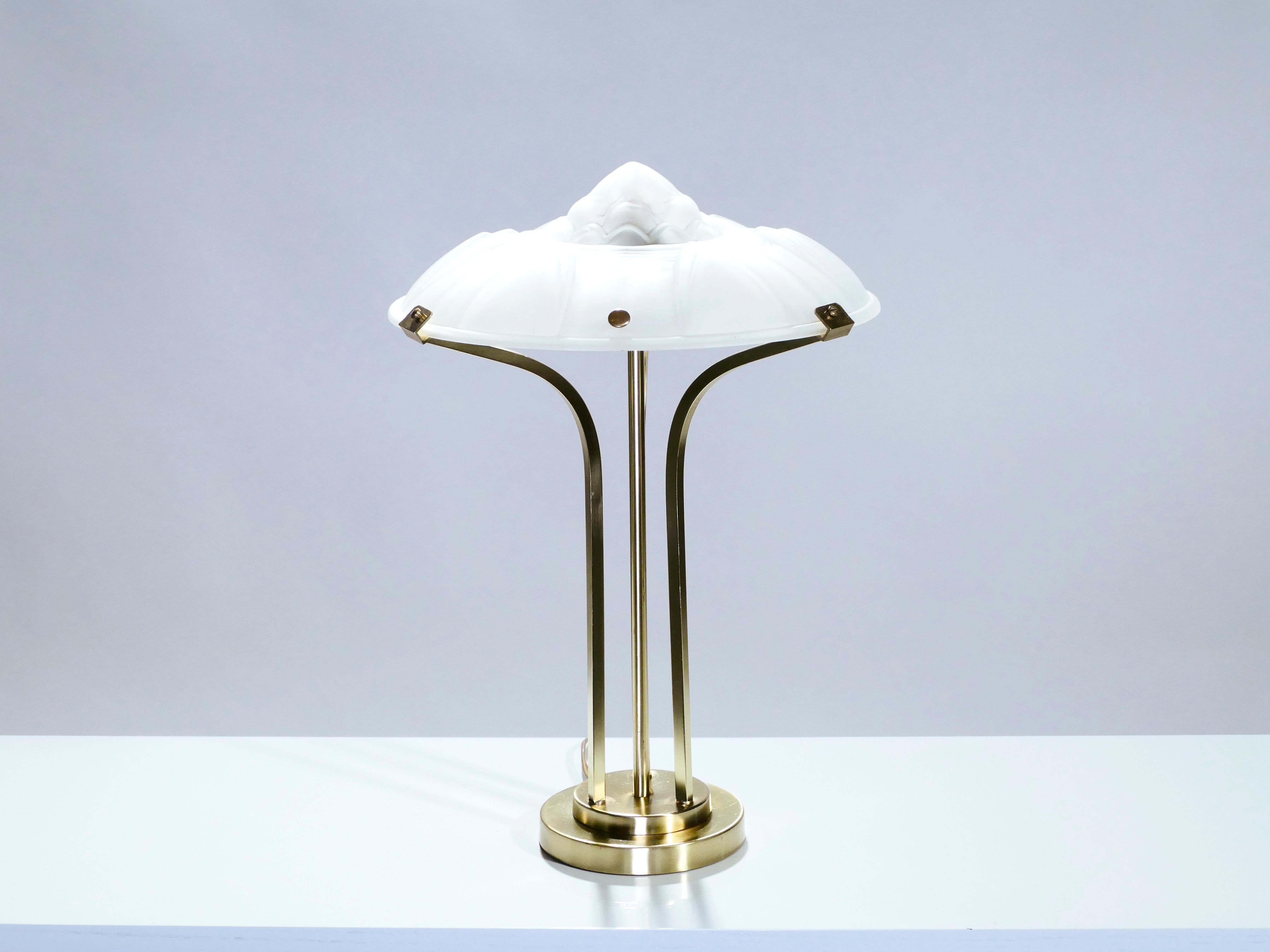 This Art Deco clear frosted glass lamp has a modernist appeal. Brass forms the structure: a central straight rod flanked by two dramatically curved outer rods atop a simple tiered base. The top is made from lovely, cloudy opaline glass. The glass is