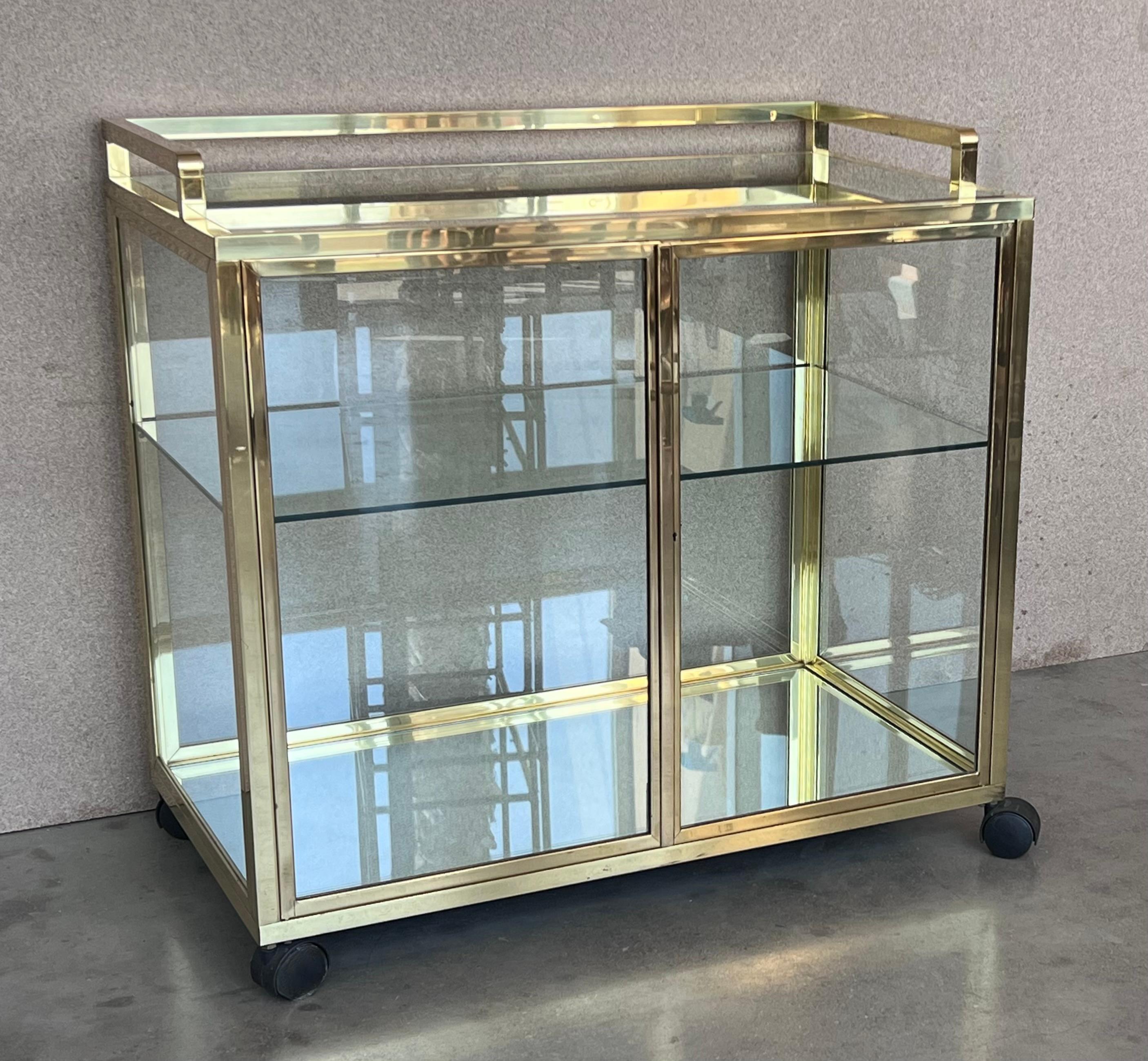Fabulous brass bar cart with enclosed glass cabinet center. 
The has one middle shelve and the base shelve is made of mirror. 
Proudly showcase your finest decanters and stemware! Brass handle. 
2 sliding glass panel doors in front. 
 This piece
