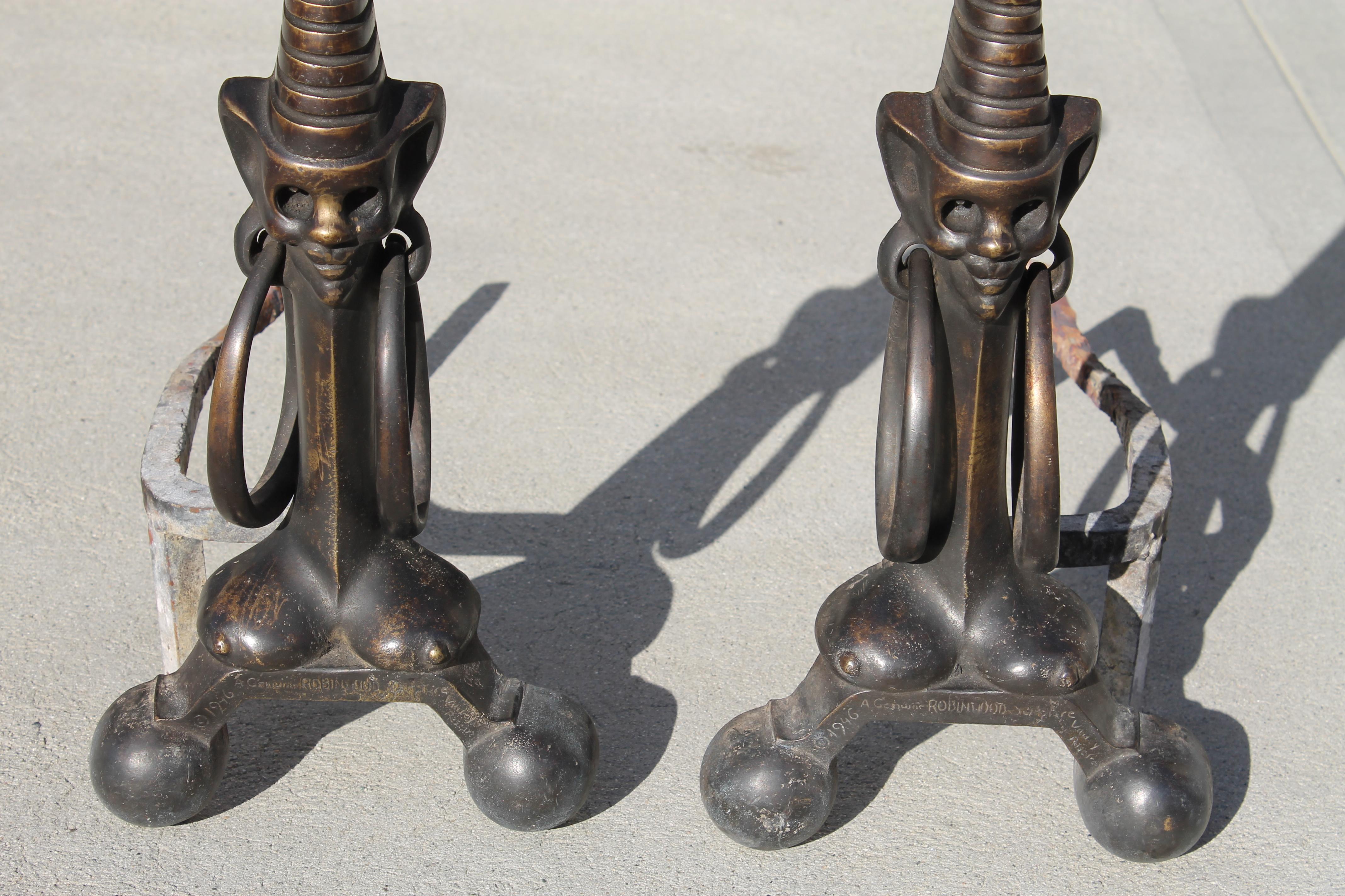 An unusual pair of mid century modern (circa 1940s) solid bronze andirons in the form of stylized African figures with giant hoop earrings. Early Hollywood Regency style. These are marked (Copyright) 1946, a genuine robinwood sculpture, then a name