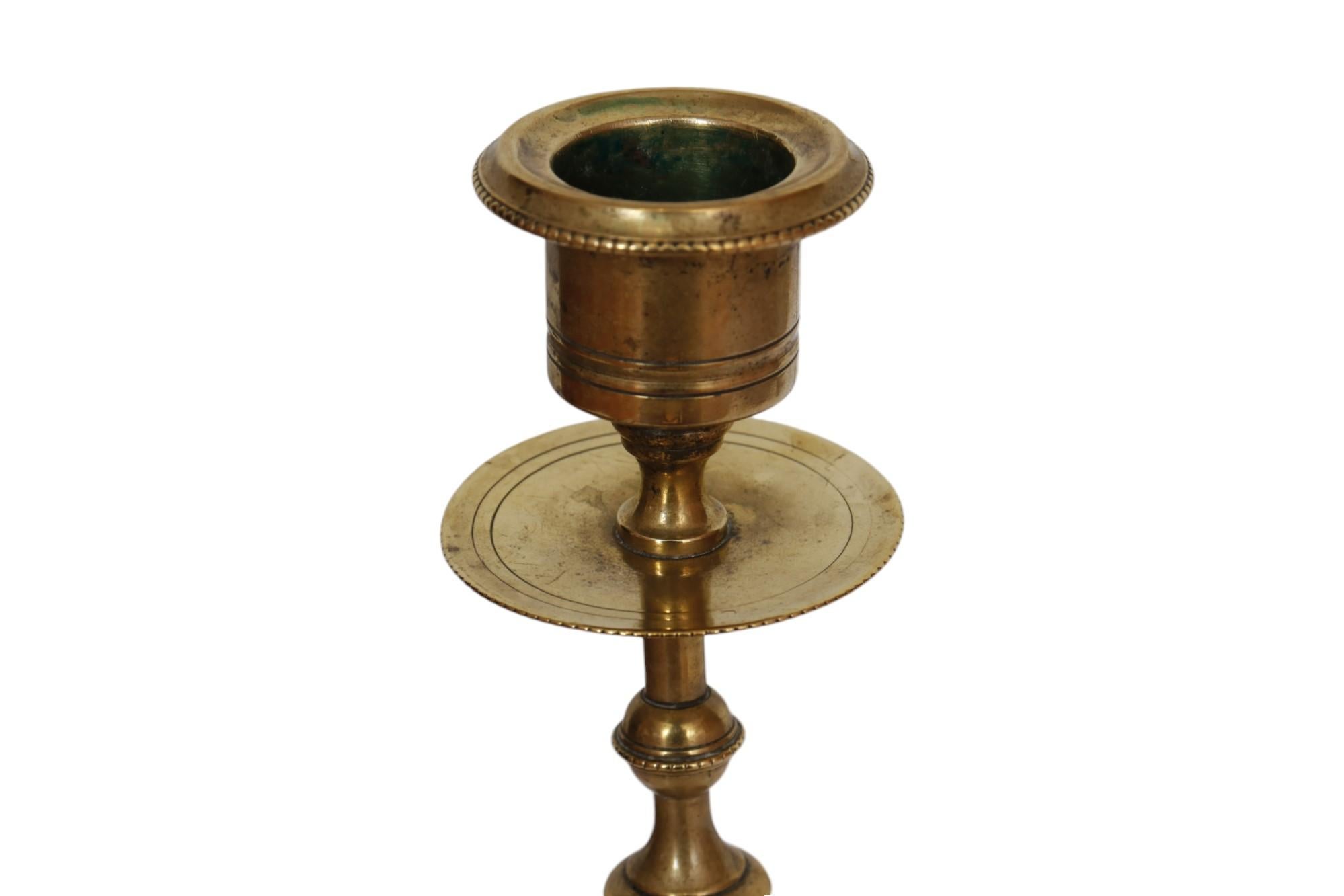 A pair of Art Deco period brass candlestick holders. Delicately turned stems are decorated with palm leaves and beaded knops, with fine drip pans and beaded sconces. The beveled base is finished with gadrooning and an egg and dart motif. Dimensions