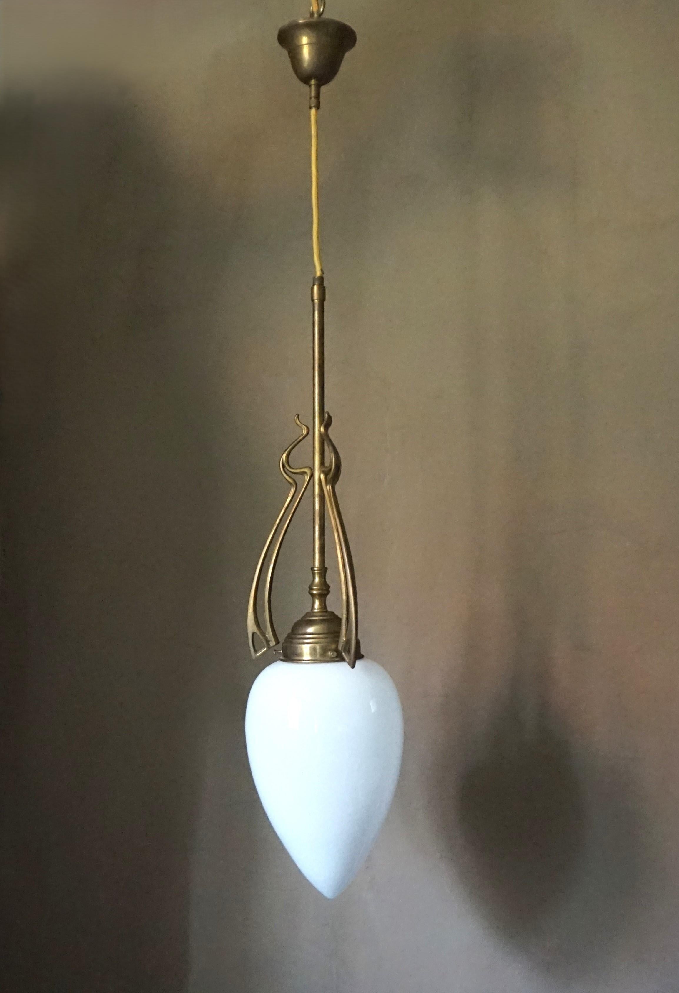 Lámpara de techo Art Decó de latón macizo en excelente estado. El marco de latón presenta una atractiva pátina y está diseñado con bellas líneas Art Déco. Apenas muestra signos de desgaste. El cristal opalino en forma de gota no muestra signos de