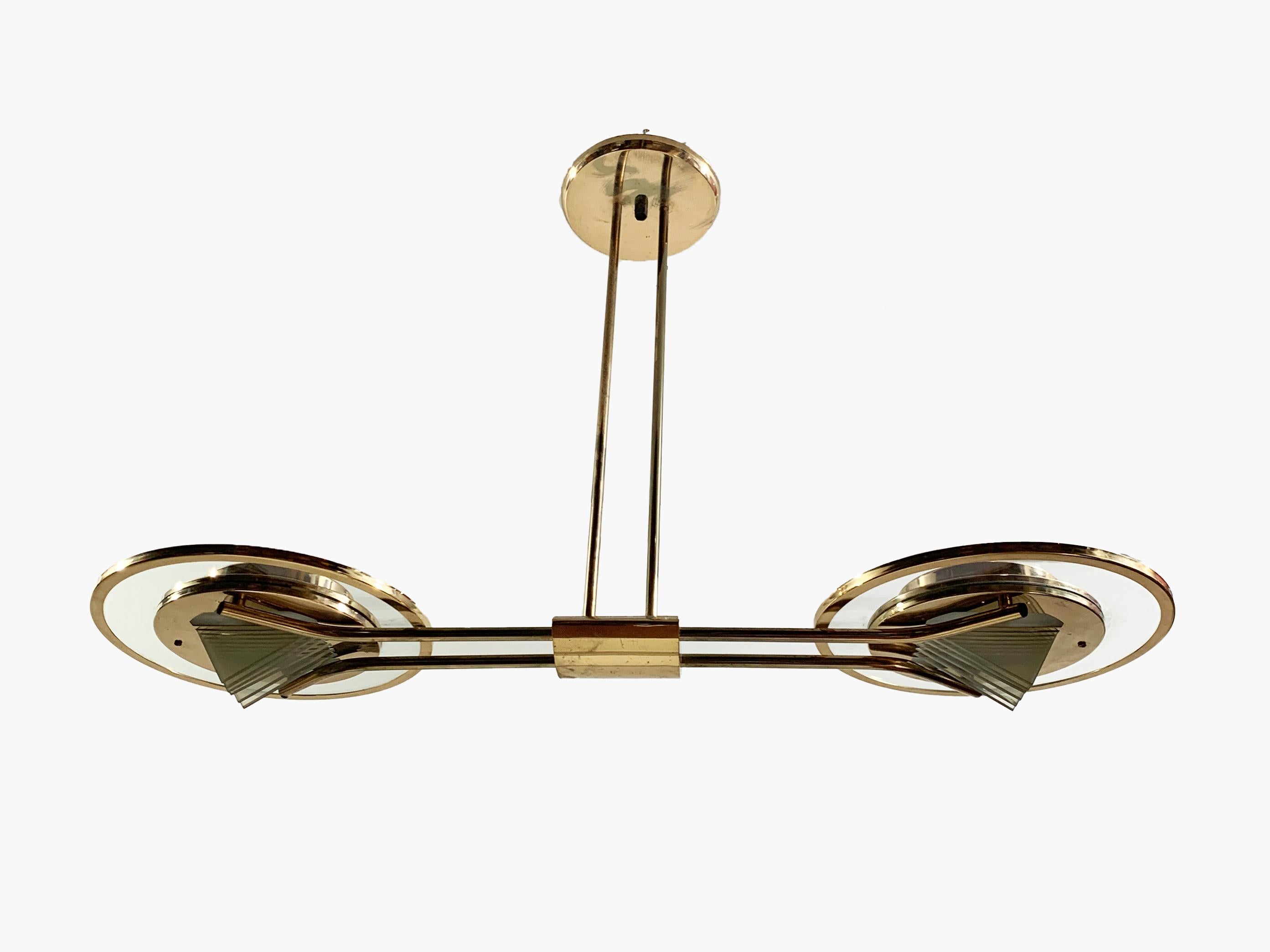 Esempio di design moderno di metà secolo, questo lampadario scultoreo presenta un'elegante struttura in ottone accentuata da eleganti paralumi circolari in vetro. L'apparecchio centrale è sospeso da un baldacchino rotondo sul soffitto tramite due
