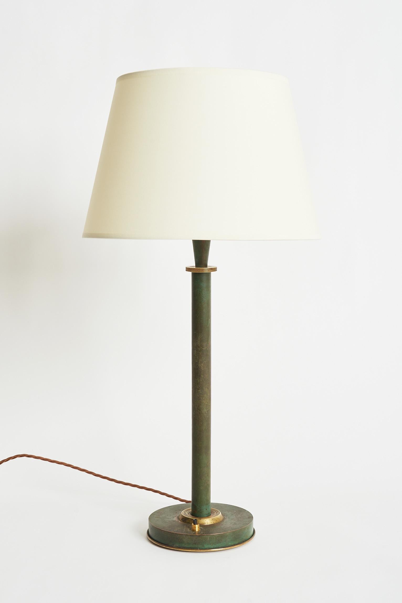 A brass mounted green patinated brass table lamp.
France, Circa 1940.
Withteh shade: 71 cm high by 35 cm diameter.
Lamp base only: 51 cm high by 17 cm diameter.