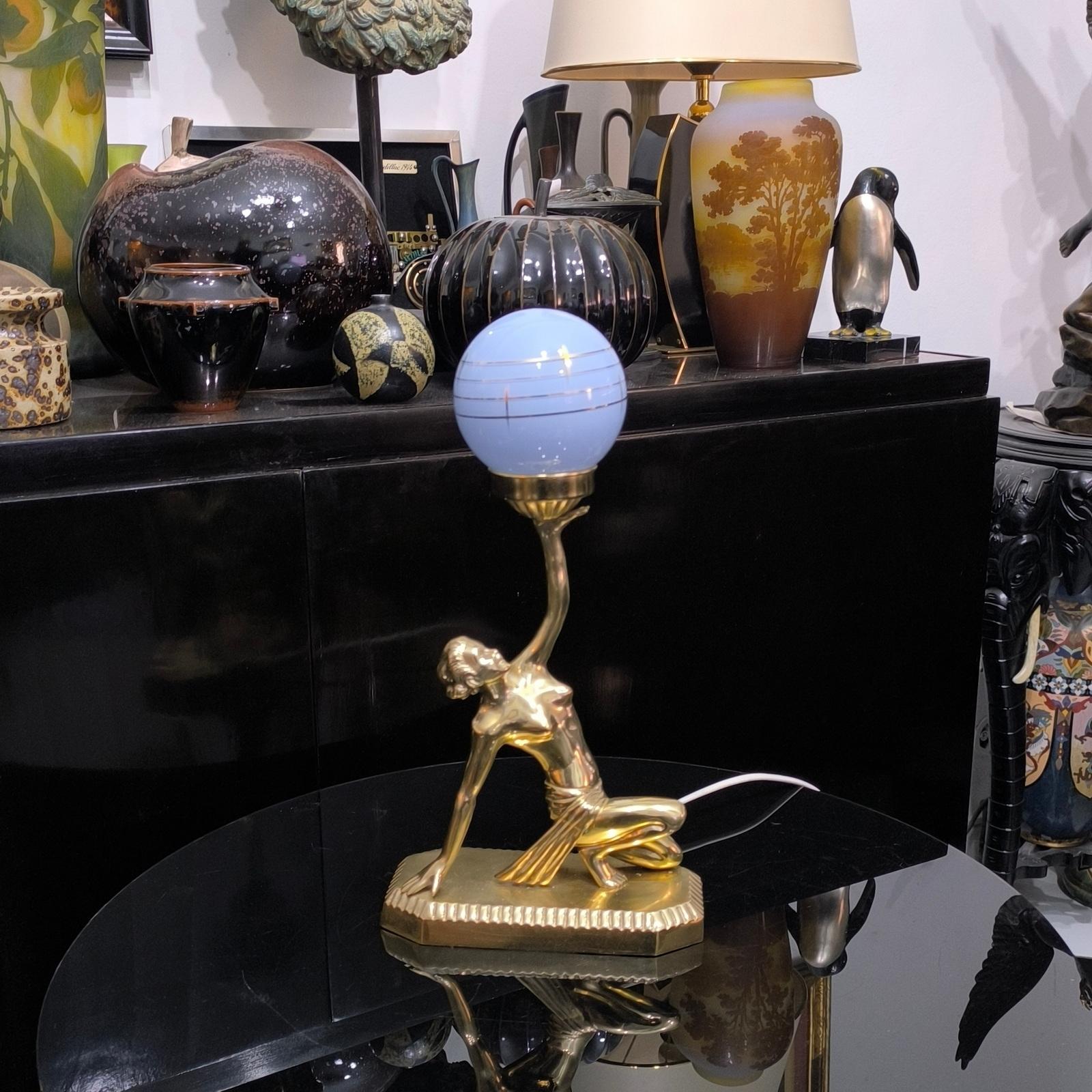 Beautiful Art Deco table lamp depicting a nude girl holding a globe.
The figure is made of brass, the globe is made of milky and blue glass, decorated with gold accents. Excellent details. Illuminated with an E14 light bulb, we can replace it on