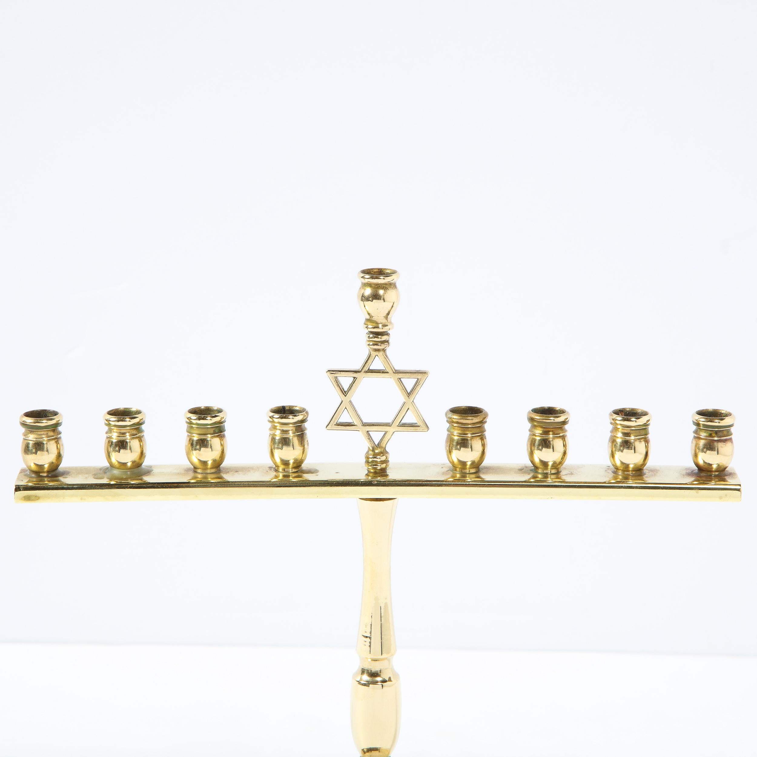 This heavy brass Art Deco menorah features a streamlined design of a stylized balustrade form support on a tiered circular form base . It features 9 candle holders in the form of styled oil vessels ,the central one being supported by a star of