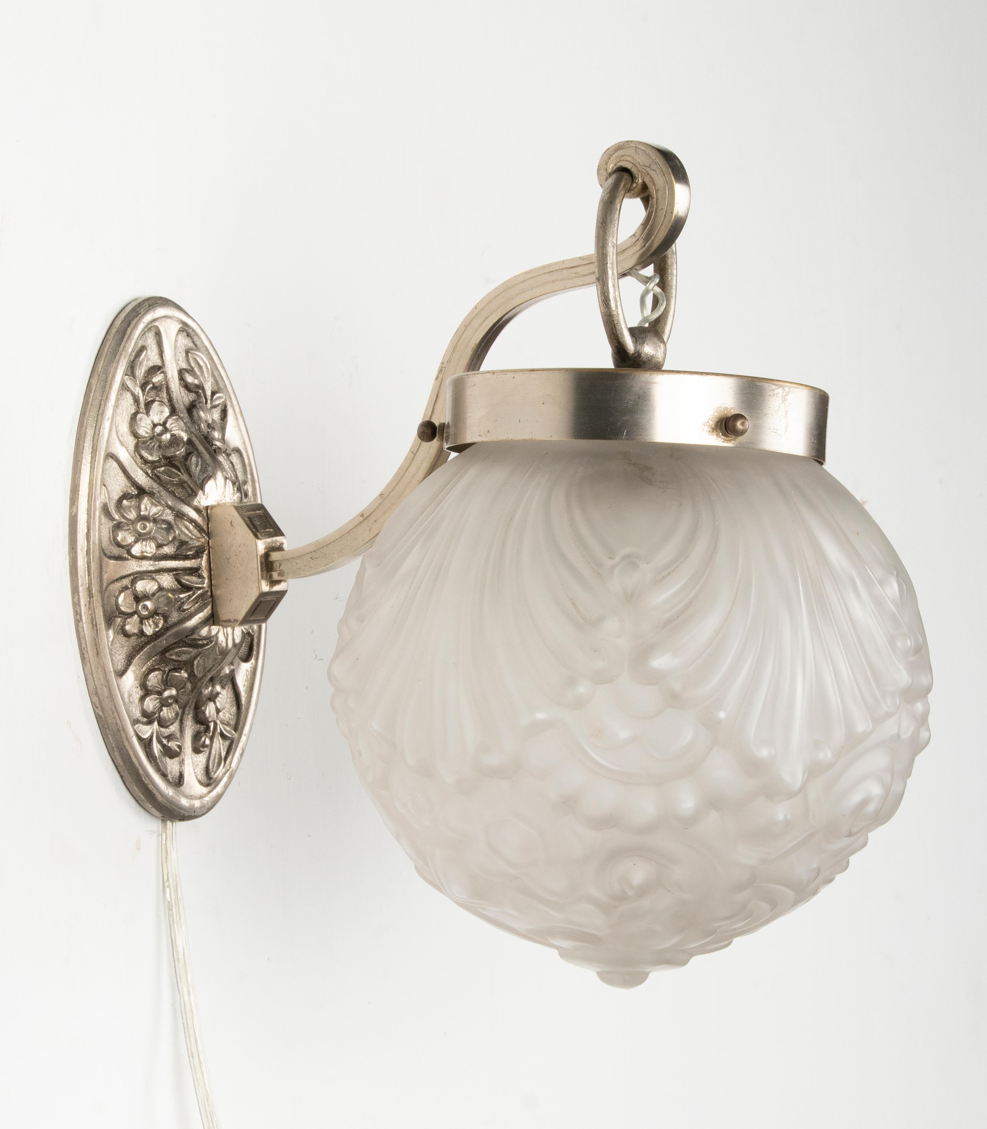 A small but stylish wall lamp made of nickel-plated brass. The wall support has a floral motif in pure Art Deco style. The lamp is signed on the back: L.B. 