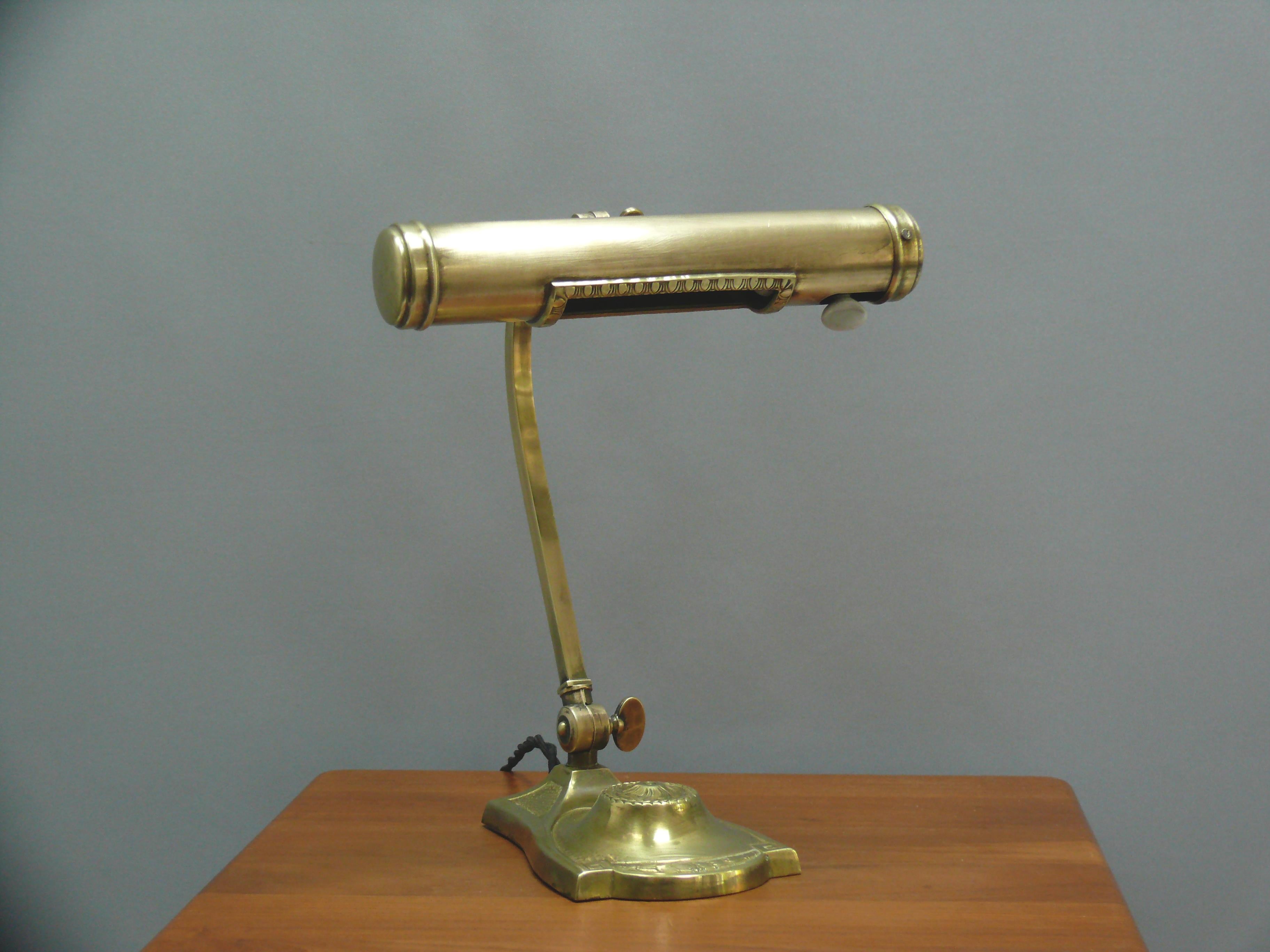 Exceptional Art Deco piano lamp/desk lamp, probably from the 1920s, featuring a decorated shade opening and a curved cast brass base. The lamp is made of brass and has a heavy, ornate stand. The shade can be tilted, and additionally, the arm can be