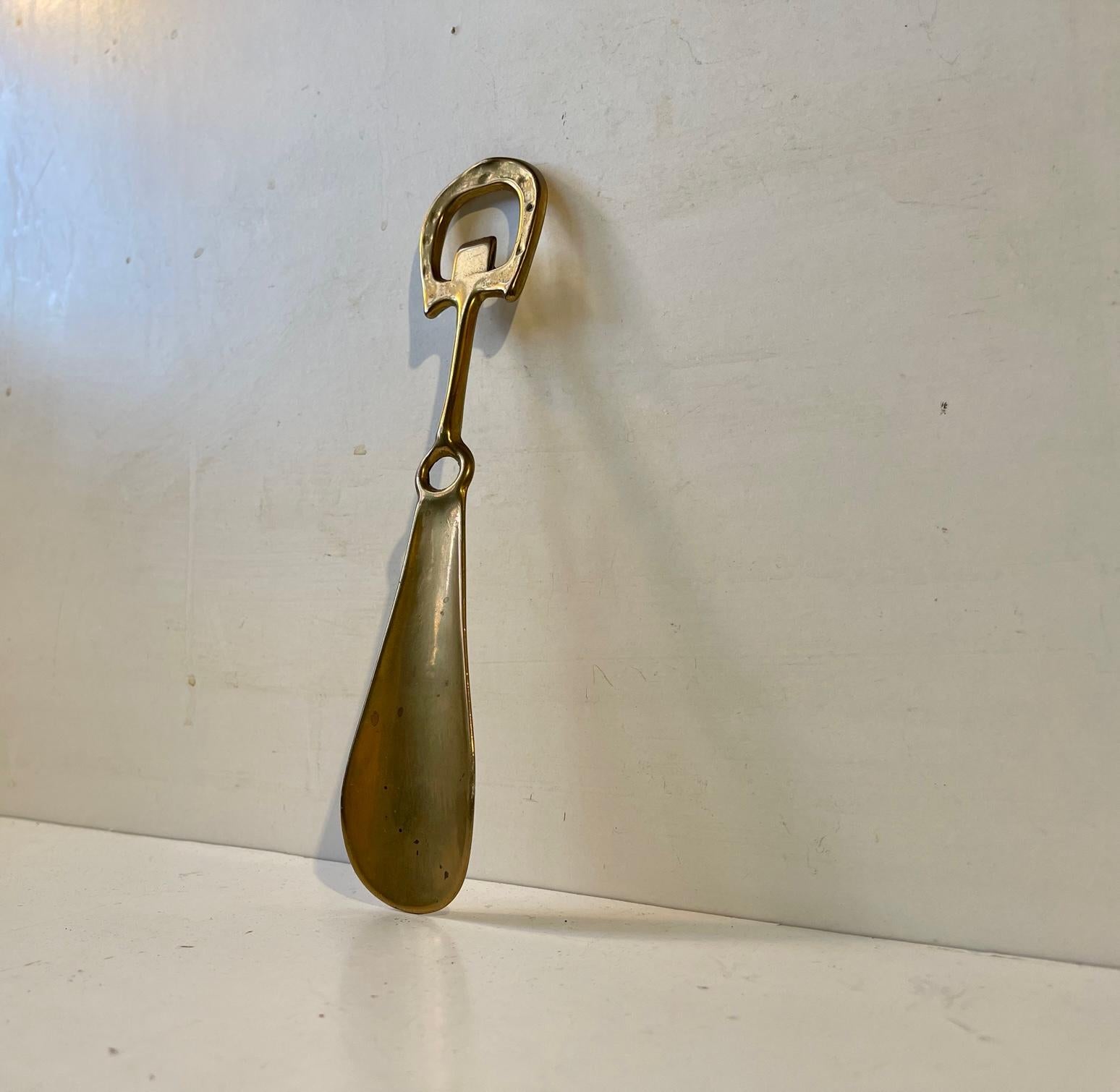 Elegantly combined shoe horn and bottle cap opener in brass decorated with a horseshoe top. It can be wall hung in your entrance. It was made in Denmark circa 1930-1940, probably by N. Jal or N.D.R. Measurements: l: 22 cm, w: 4 cm.