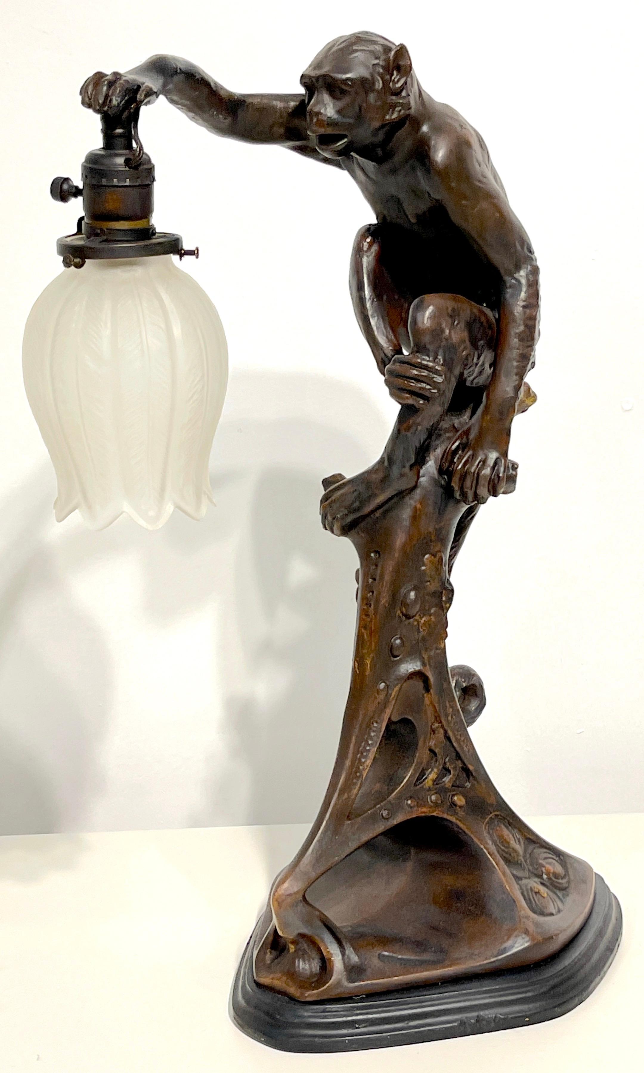 Art Deco bronze clad monkey motif table lamp, Austria, C. 1925 

A whimsical highly detailed sculptural table lamp, made of a plaster cast/maquette overlaid with bronze. Depicting a seated monkey holding a frosted plume motif glass shade, raised