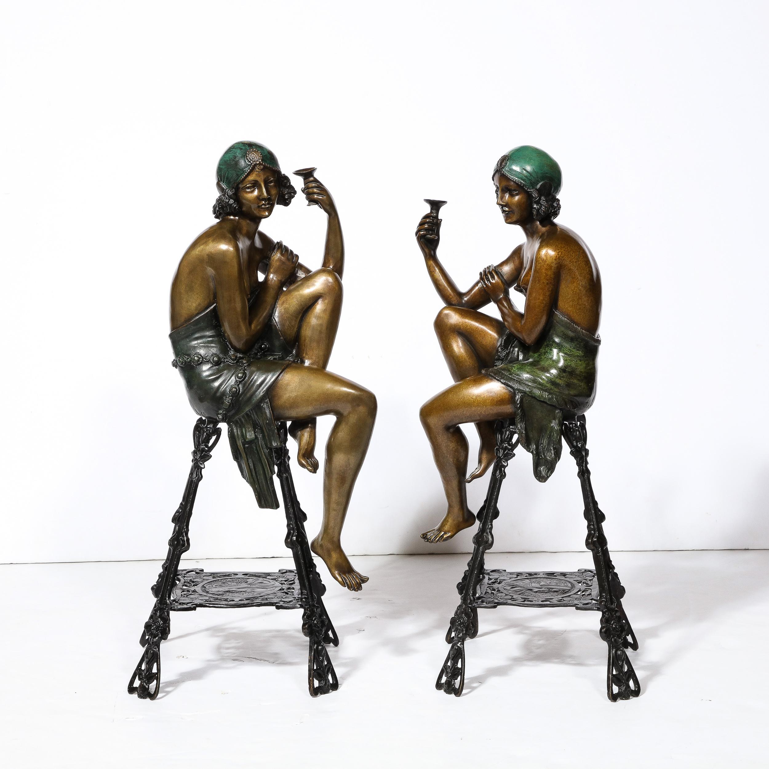 This whimsical pair of Art Deco Bronze and Copper Sculptures of Seated Women by Ferdinando De Luca originate from Italy during the dawn of the 20th Century. Featuring a pair of women seated on stylized Art Nouveau open framed stools, the sculptures