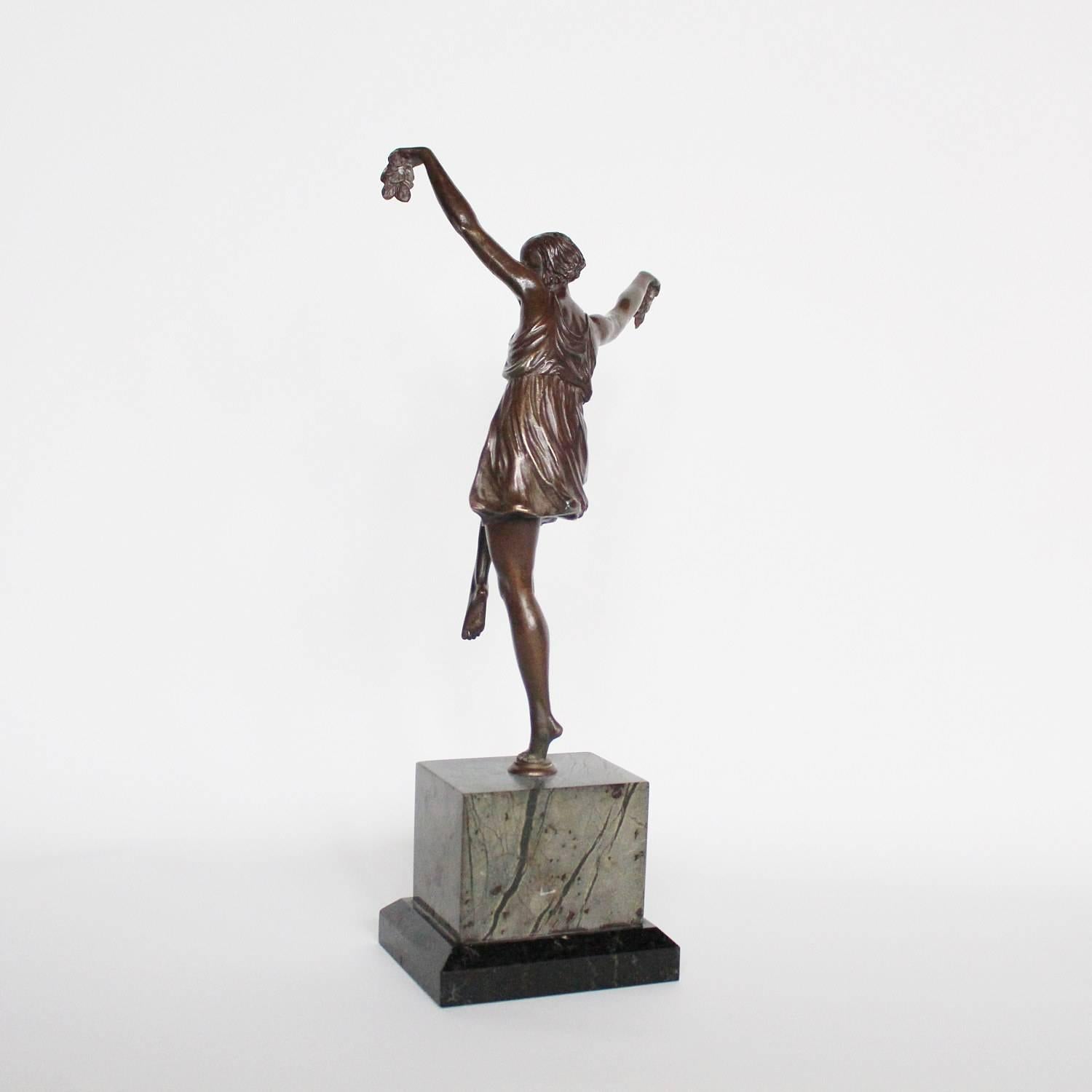 An Art Deco, patinated bronze dancer in stylised pose, holding two vine leaves aloft. Set over a bi-coloured marble plinth. Unsigned.
 
    
