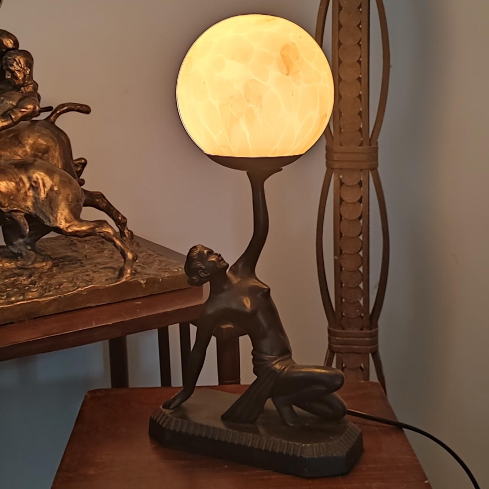 Belle lampe de table Art déco représentant une jeune fille nue tenant un globe.
La figure est en bronze, le globe est en verre marbré. Illuminé avec une ampoule E14 plus récente, nous pouvons la remplacer sur demande par une E12 pour une