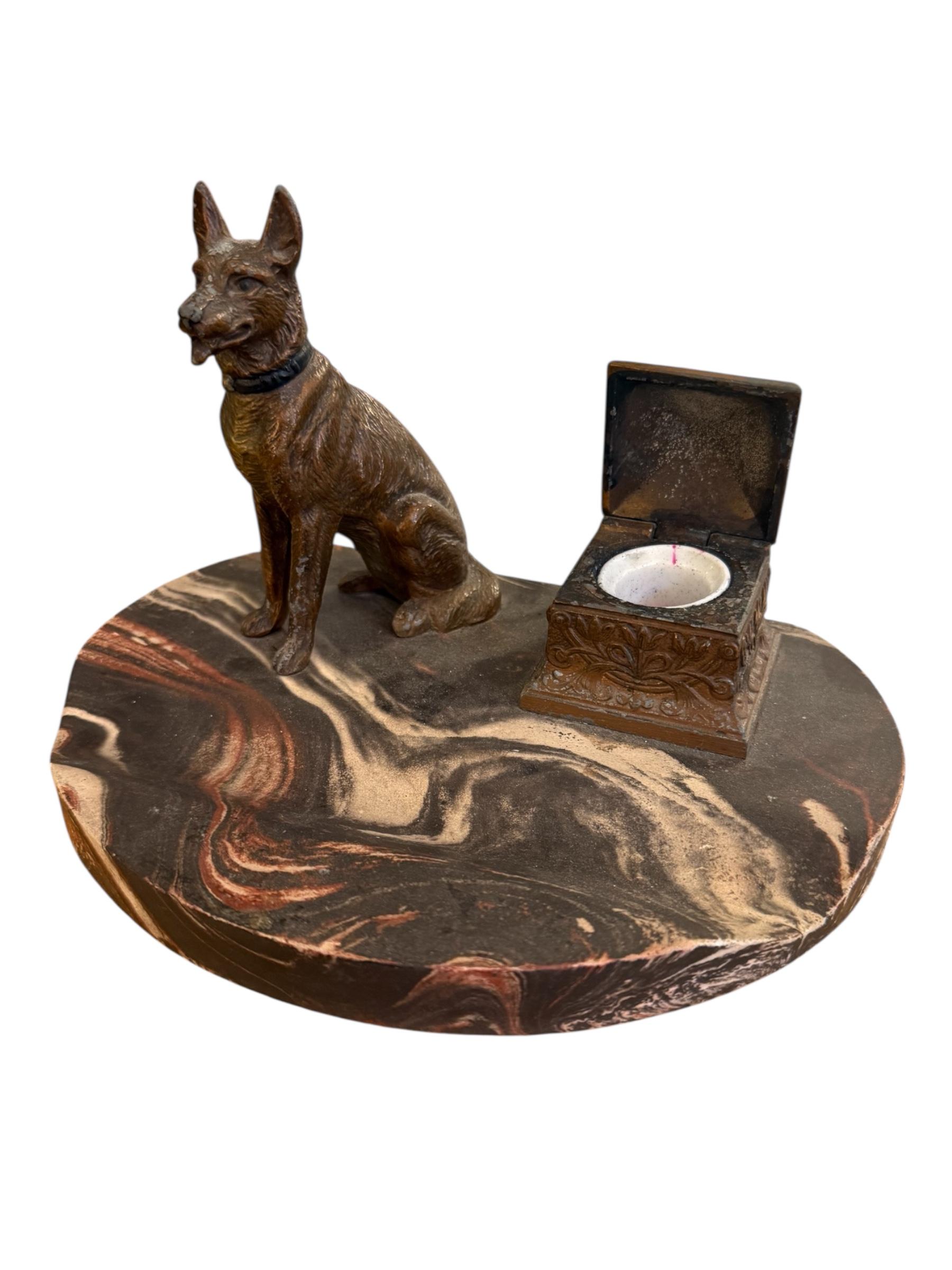 A striking blend of function and form, this Art Deco ink tray features a finely detailed bronze German Shepherd poised attentively atop a richly veined marble base. Beside the noble canine figure sits an ornate inkwell, beautifully embossed with a