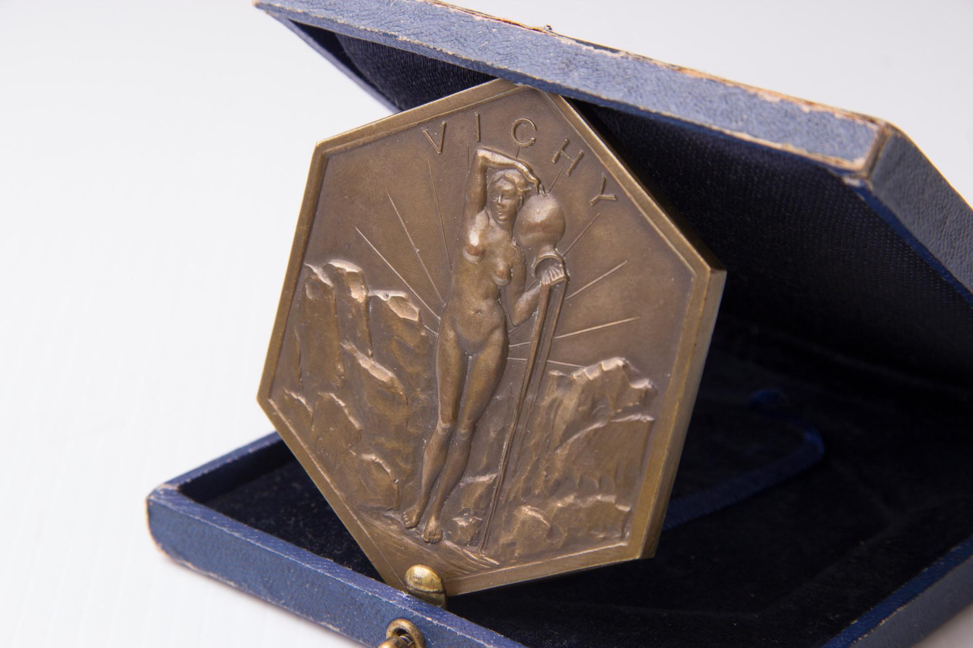 Art Deco boxed bronze medal, Vichy, depicting a nude female pouring water in a rocky landscape with sun-ray's, inscribed Cam lower left.
Measures: H 10 cm, W 10 cm, D 2 cm,
French, circa 1930.