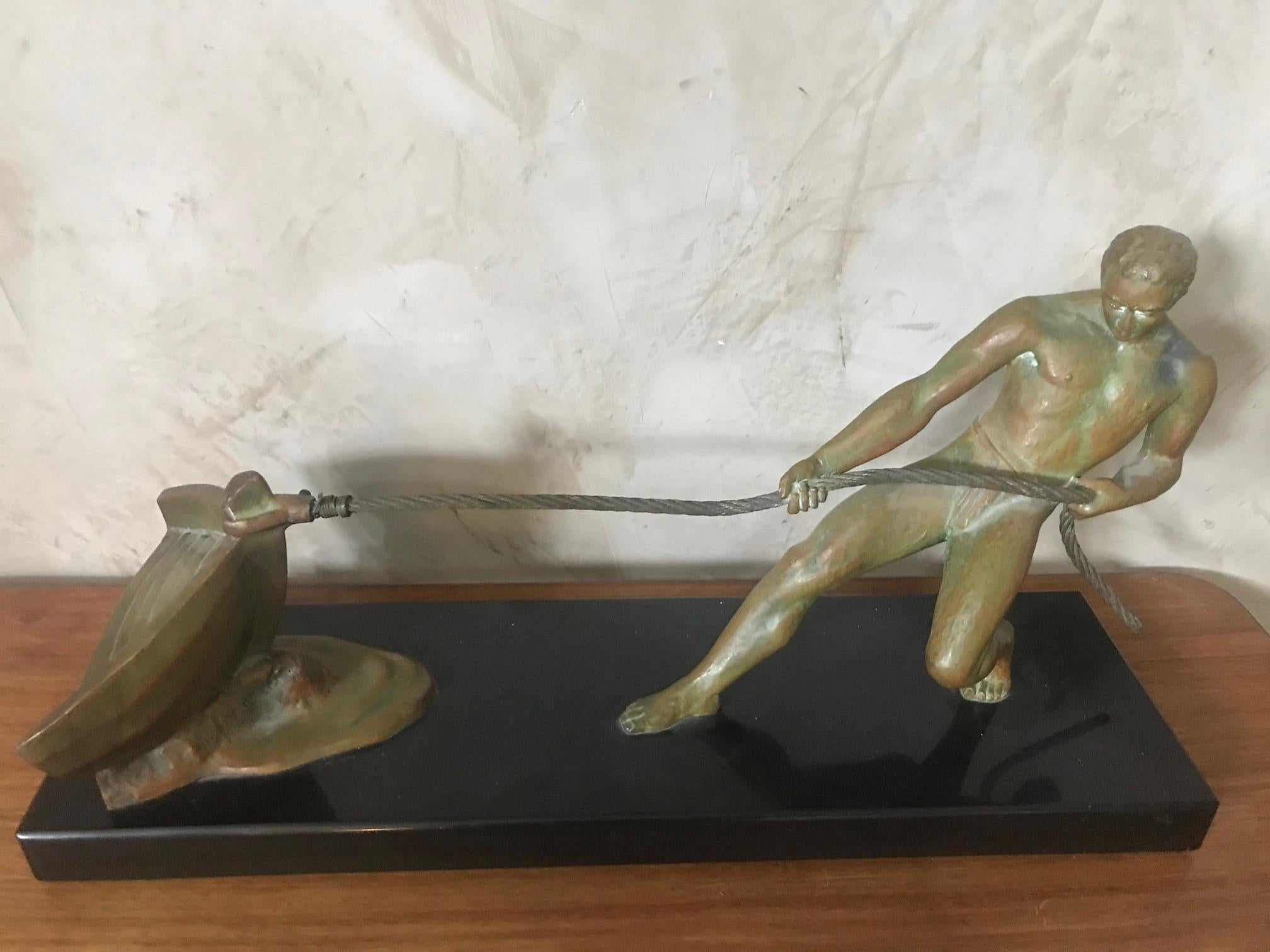 An Art Deco bronze sculpture by Salvador Riolo: of a man gripping a rope and pulling a rowboat ashore, It is a strong and unusual image, in contrast to the many images of men throwing spears or bending steel, this uses a section of the boat to