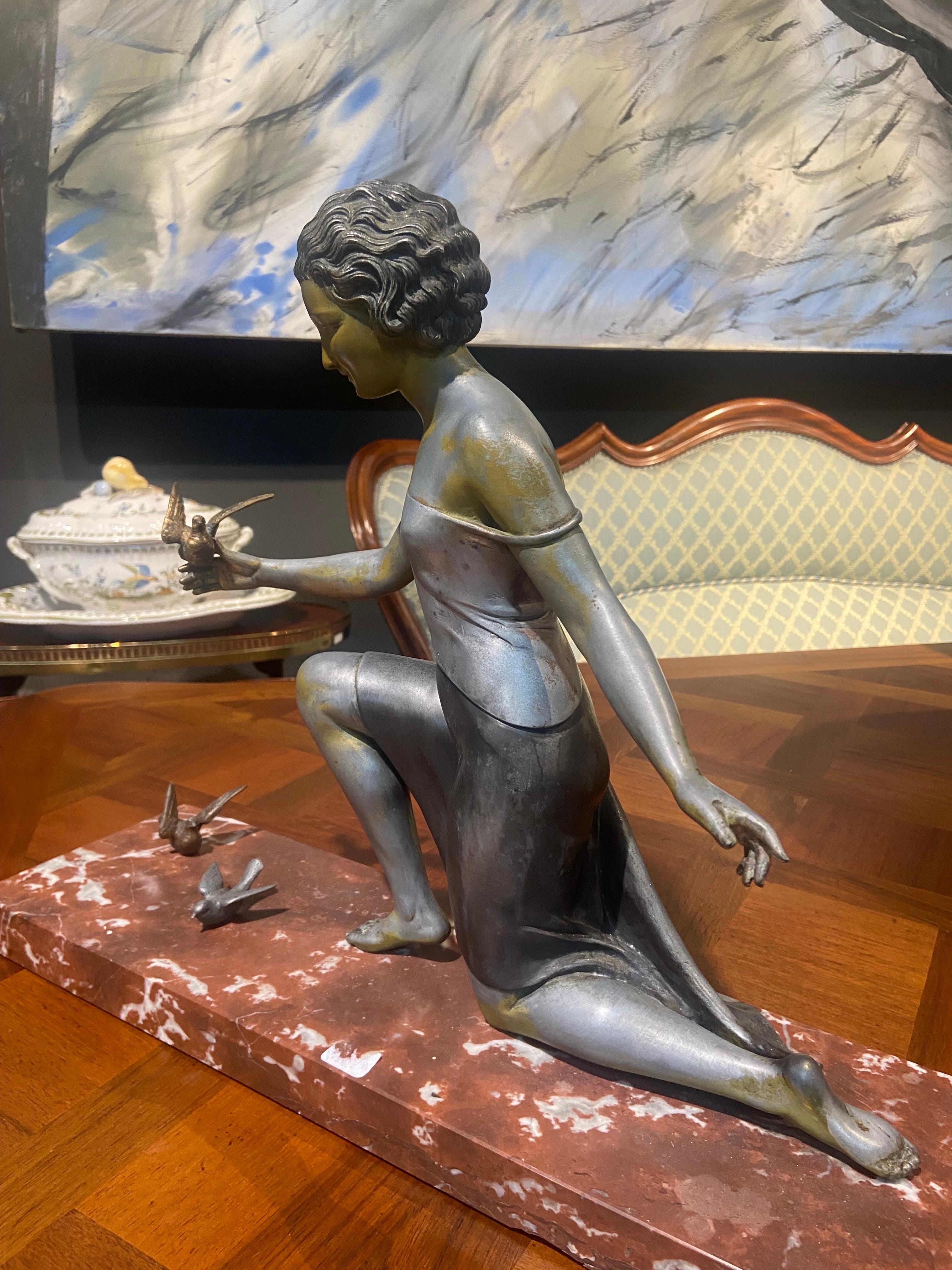 Sculpture en bronze sur socle en marbre rouge représentant une jeune femme avec des oiseaux. Elle a été réalisée et signée par l'artiste italien Ugo Cipriani qui a longtemps travaillé en France. Cette sculpture a probablement été réalisée vers