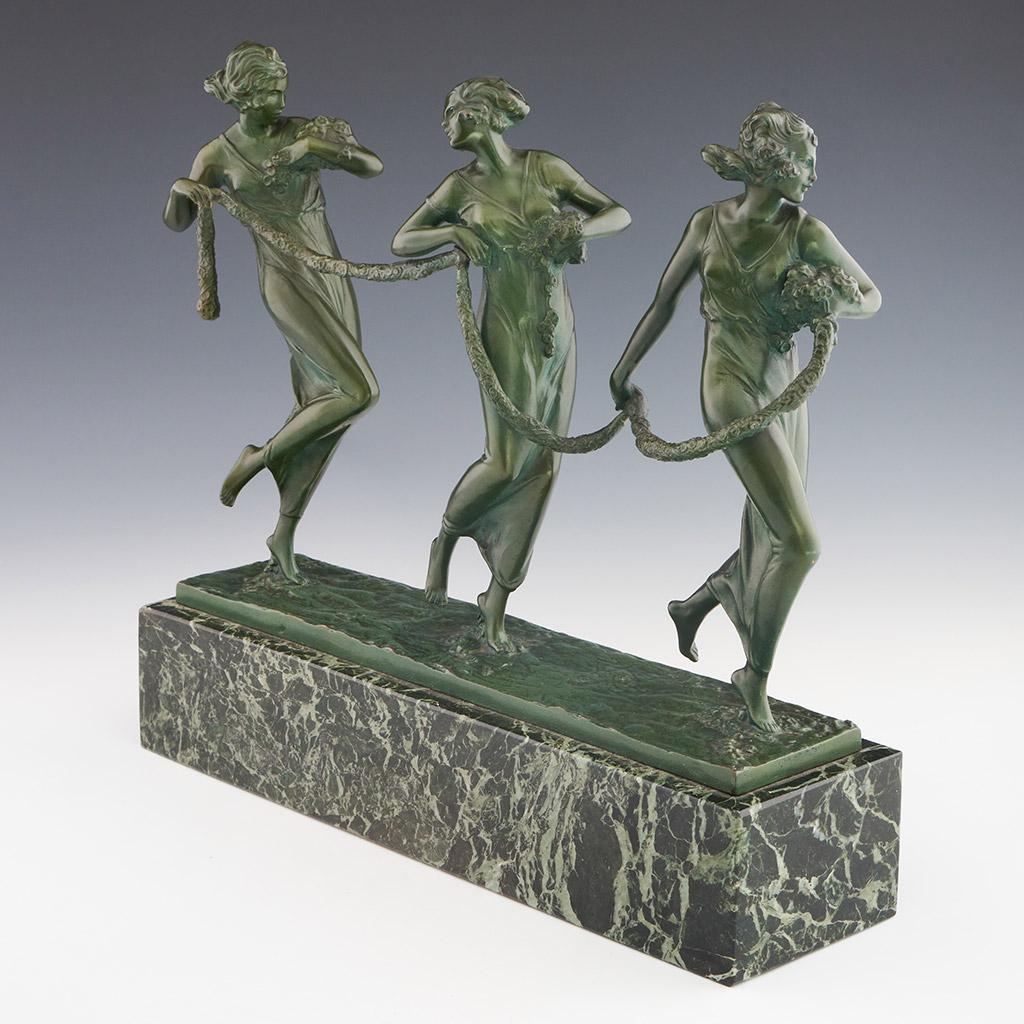 An Art Deco bronze sculpture by Bruno Zach depicting the three daughters of Zeus, playfully dancing with a garland of flowers between them. Rich green patination, set over a marble base. Signed to bronze. 

Dimensions: H 34cm W 37cm D