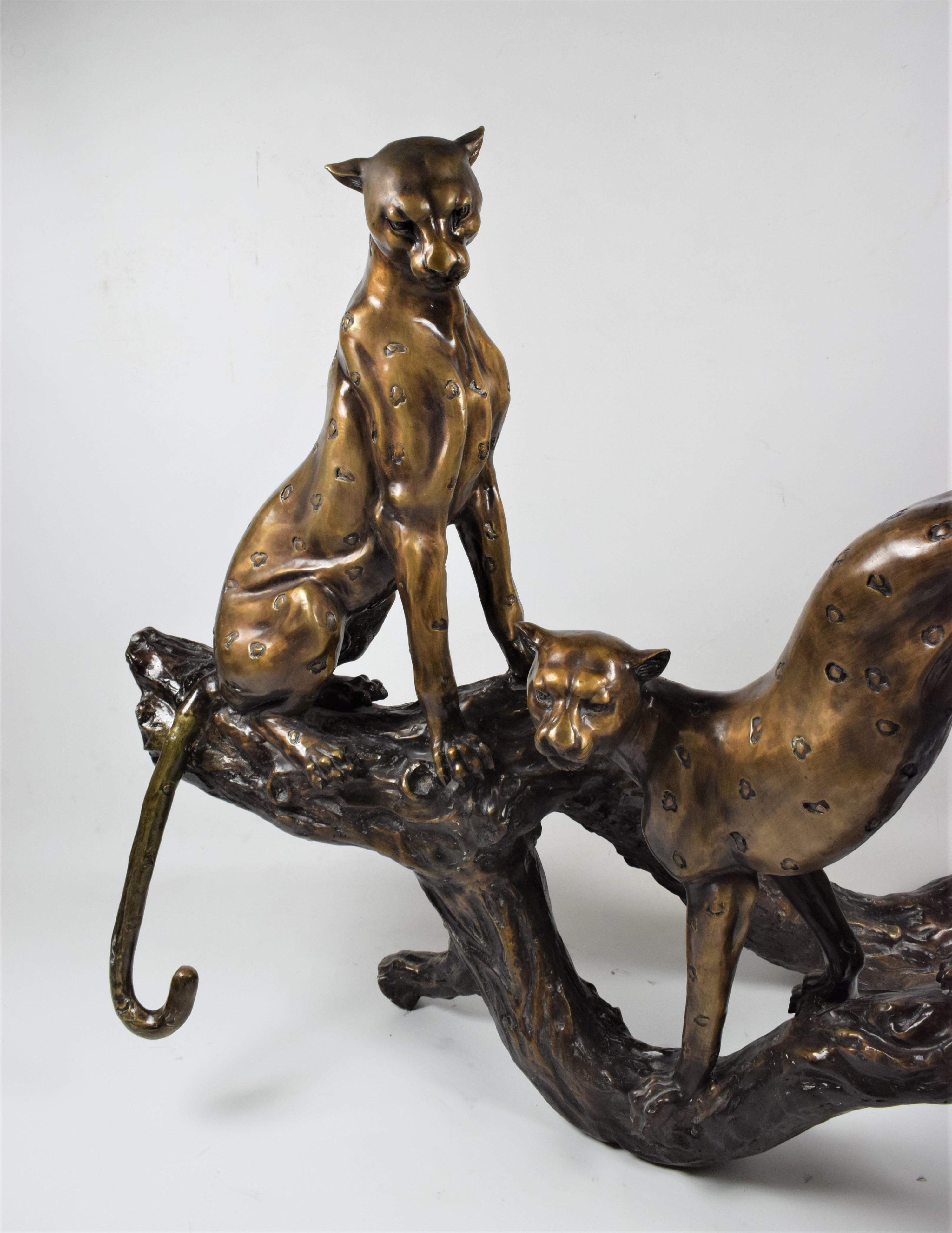La sculpture art déco en bronze représente une scène captivante mettant en scène deux guépards dans une pose détendue mais alerte, perchés sur un tronc d'arbre majestueux. D'une facture exquise, la sculpture capture la grâce et l'élégance de ces