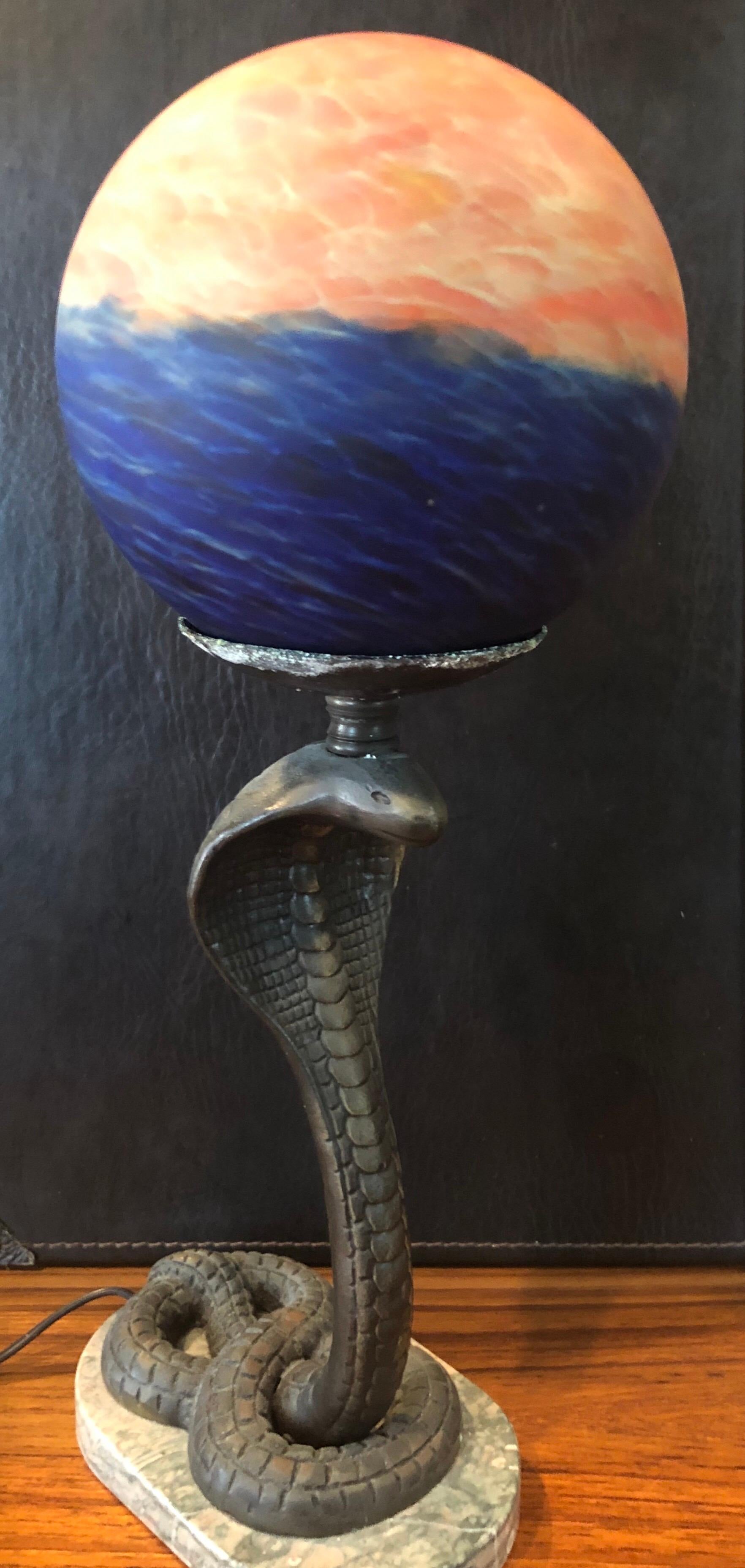 A very cool Art Deco bronze cobra / snake table lamp on marble base with colorful round globe, circa 1960s. The lamp depicts a highly detailed cobra snake in a strike position supporting a round glass globe shade. 

Specifications:
Height: