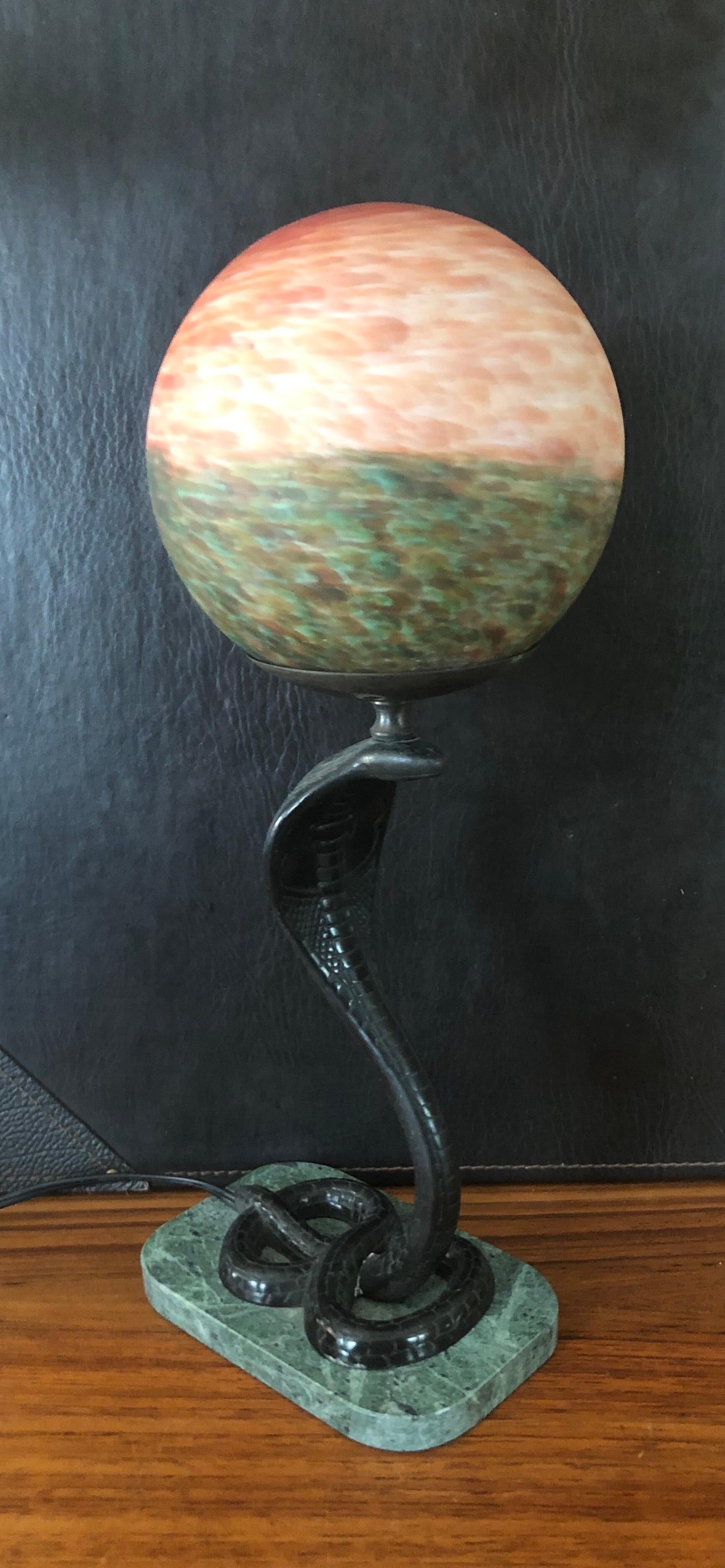 A very cool Art Deco bronze cobra / snake table lamp on marble base with colorful round globe, circa 1960s. The lamp depicts a highly detailed cobra snake in a strike position supporting a round glass globe shade. 

Specifications:
Height: