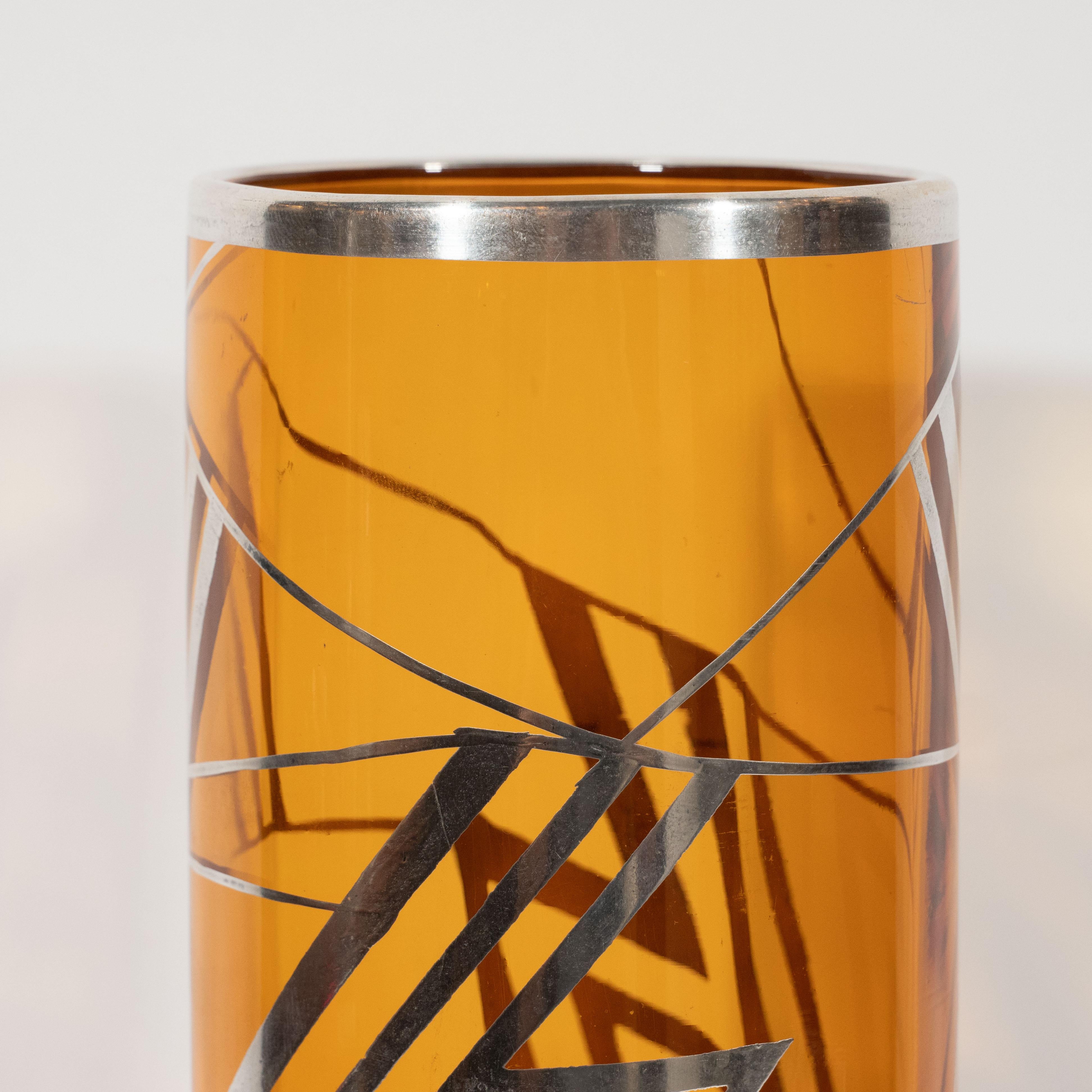 This beautiful glass vase was realized in France, circa 1935. It features a cylindrical body handblown in a rich brown topaz hue with overlaid geometric cubist designs- zig-zagging lines and triangular forms- hand-painted in sterling silver