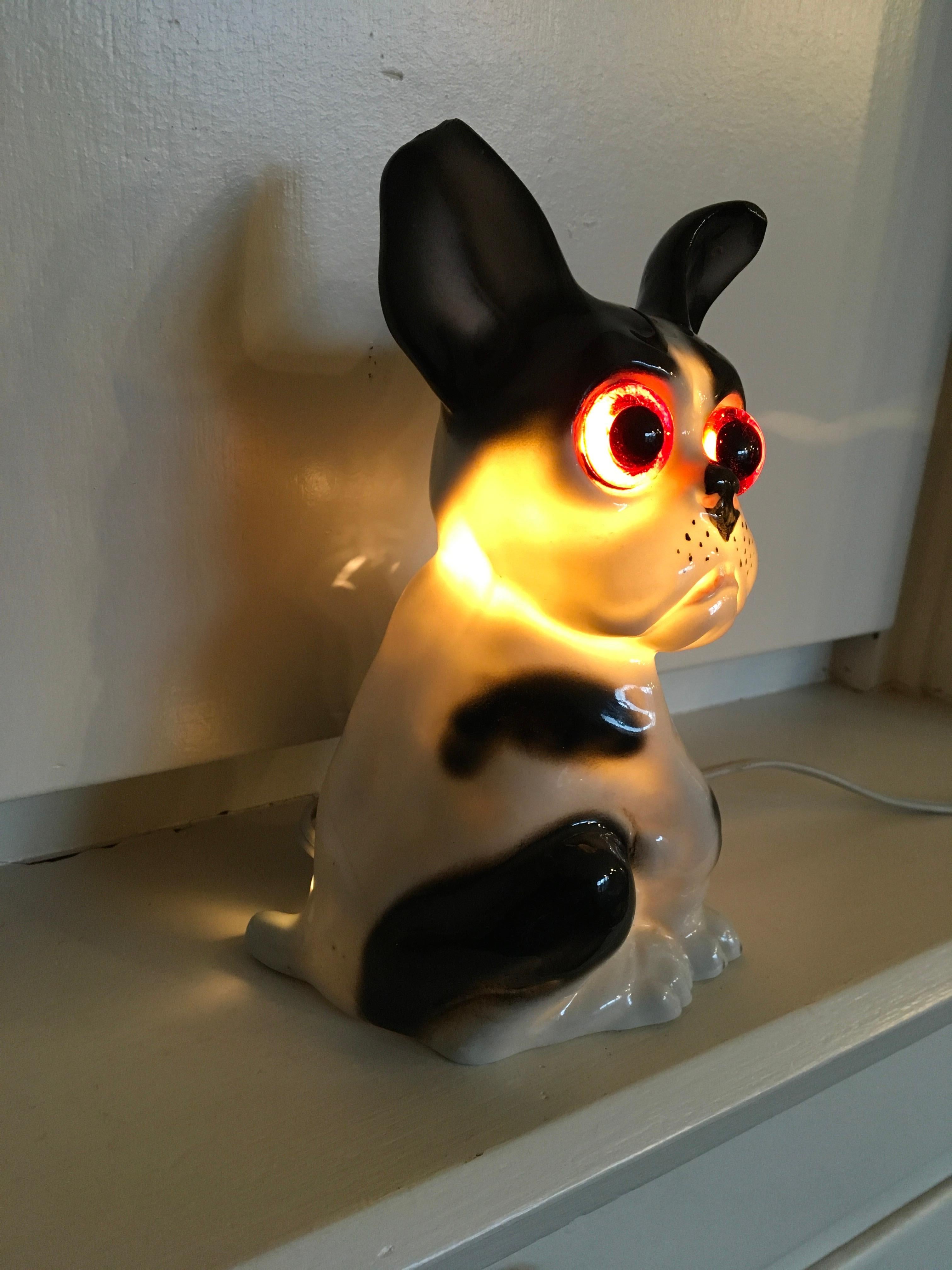 Art Deco Bulldog Perfume Lamp. 
This comical bulldog perfume light dates from the Art Deco period circa 1930s. 
It's a black and white sitting Frenchie dog, made of porcelain, with large glass orange eyes and light inside.
A collectable French