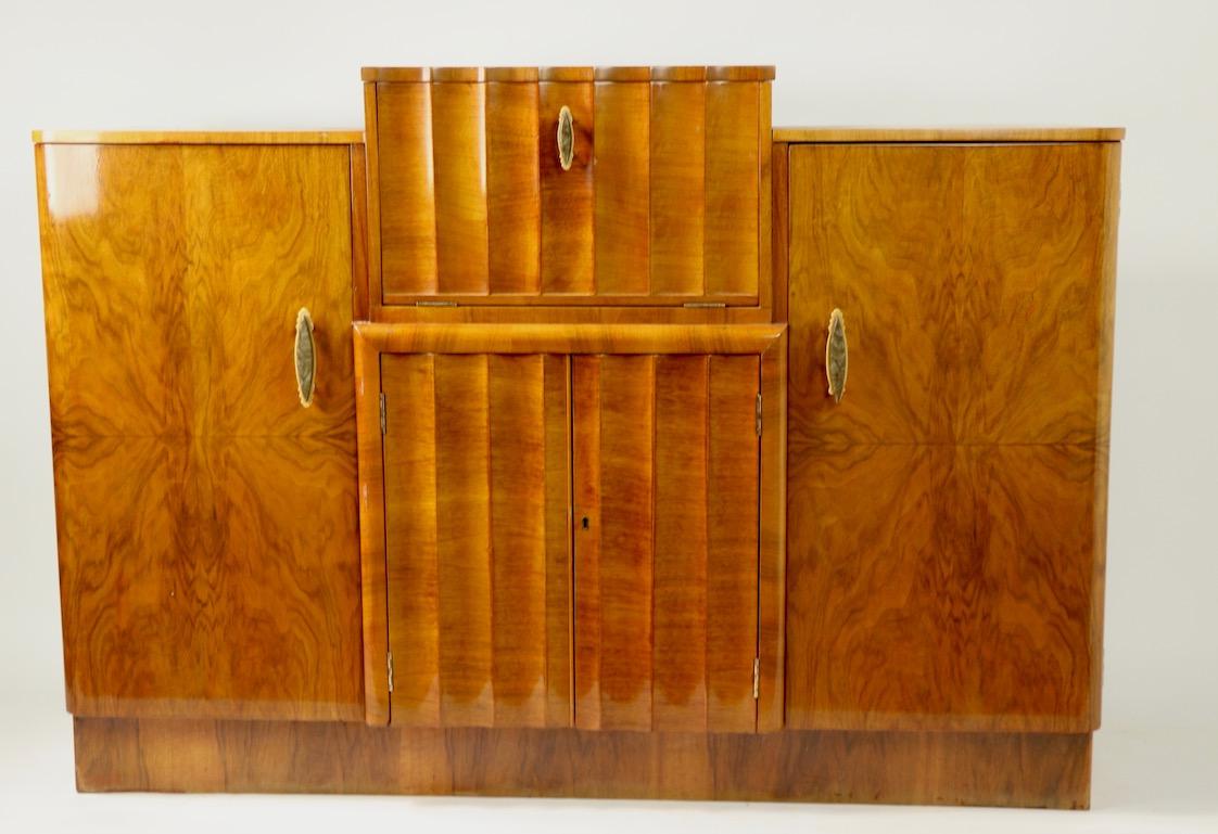 Stunning Art Deco cabinet bar having extraordinary burl veneer, marbleized Bakelite handles, and original peach mirrored interior. The center front door opens to create the work surface for preparing your favorite cocktails while the bottom and side
