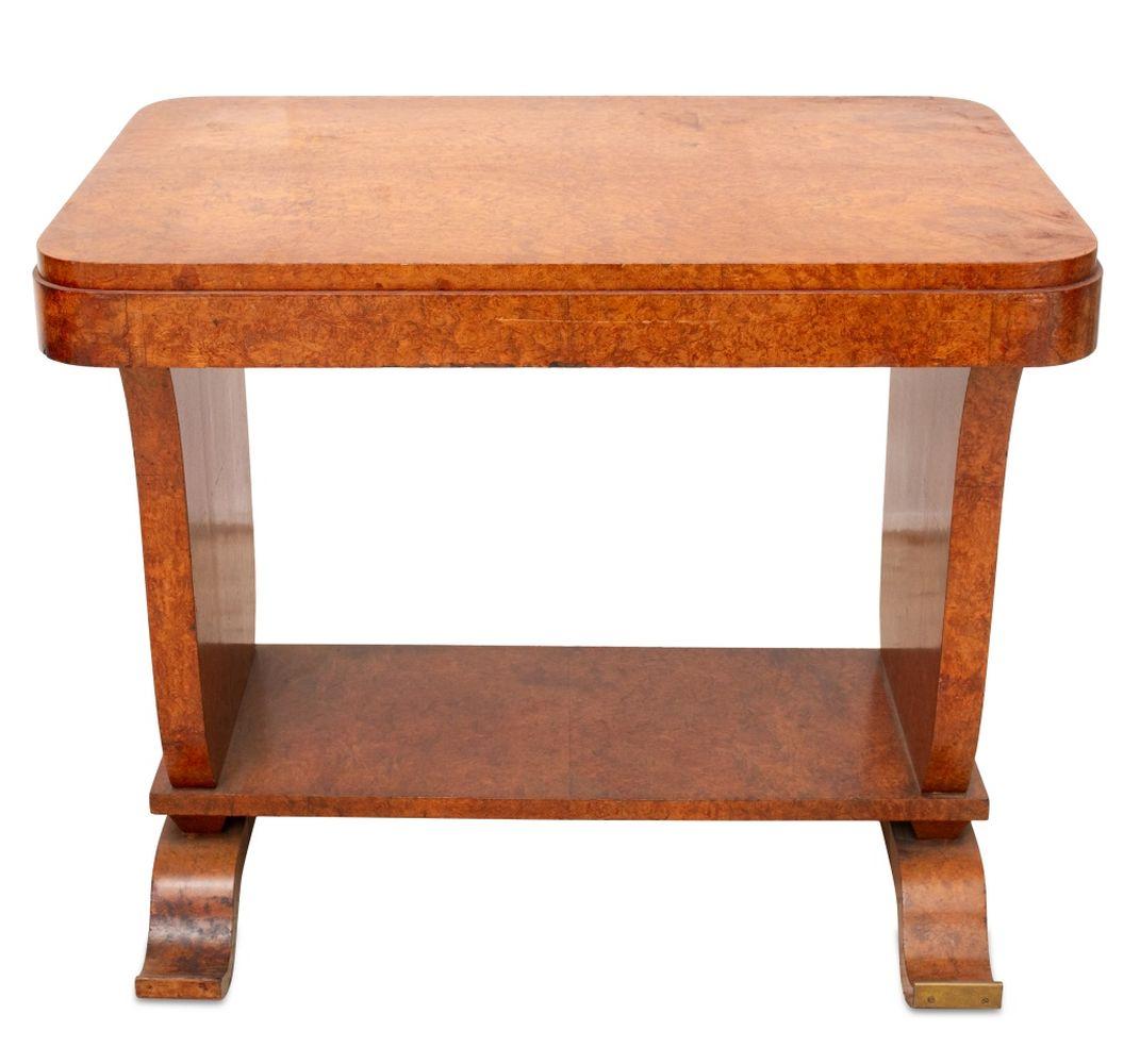 Art Deco Burl Elm Occasional Table, circa 1930, the rounded rectangular top above urn-shaped trestle and supports, with an under tier on brass mounted scroll feet. 28.5