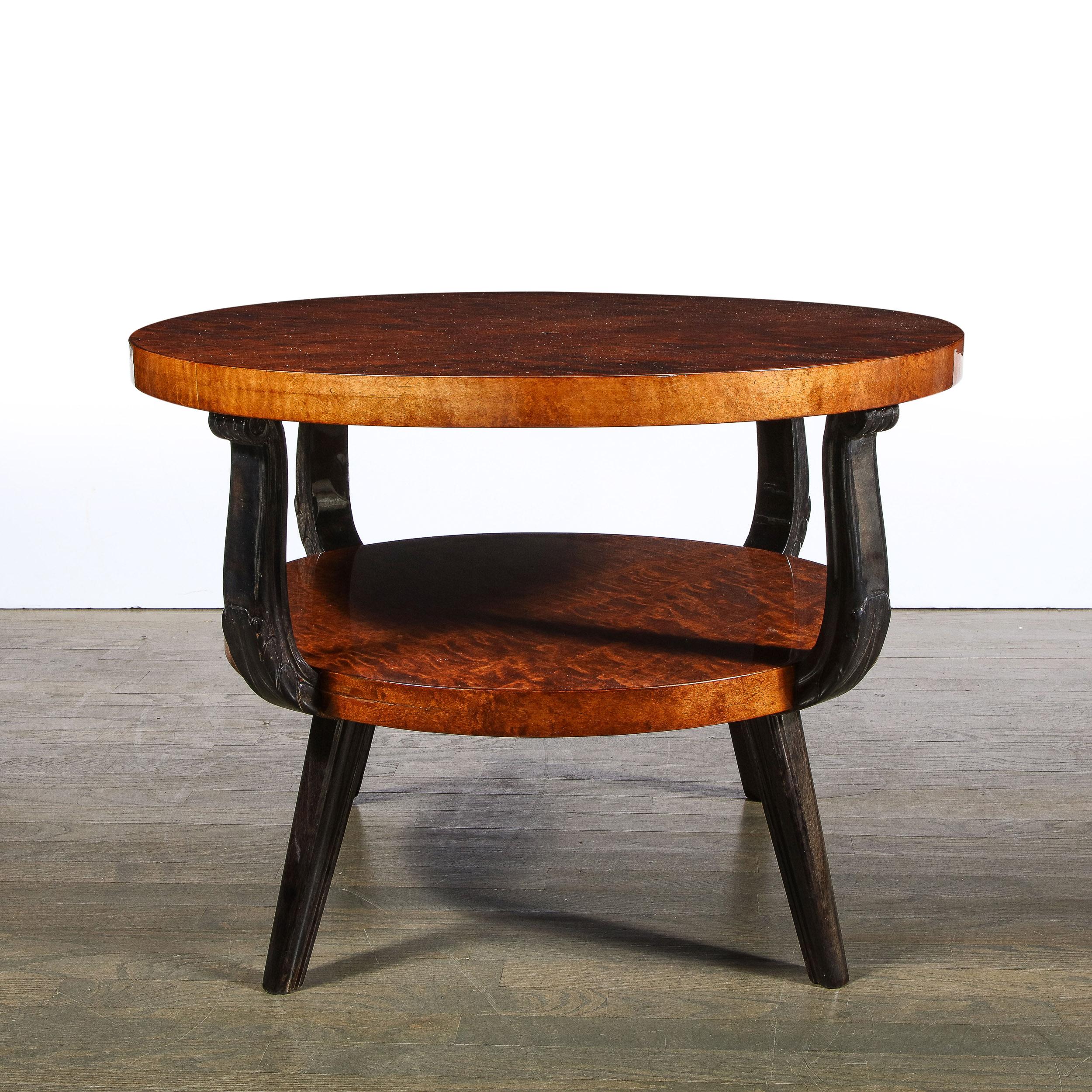 This elegant two tier Art Deco table was realized in France circa 1930. It features two circular tiers in beautiful burled acacia with splayed black lacquer legs and streamlined scroll form supports connecting the tiers. With its beautiful quality