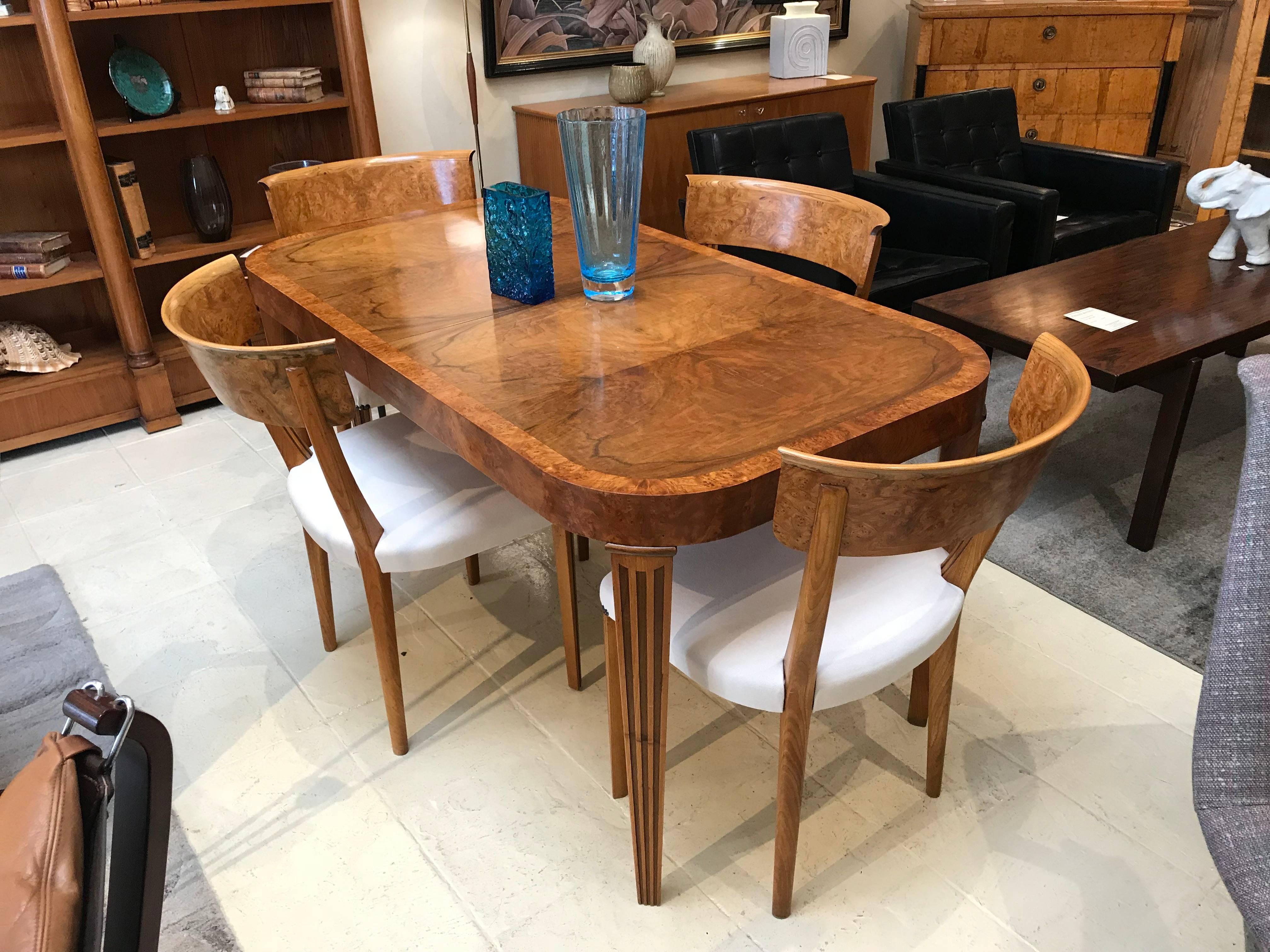 Art Deco elm and burr elm dining table with reeded legs. The table has two plain extension leaves to seat eight. The colour and burl of the timber is superb. There are four matching Clismos dining chairs which have been reupholstered in a macro sued