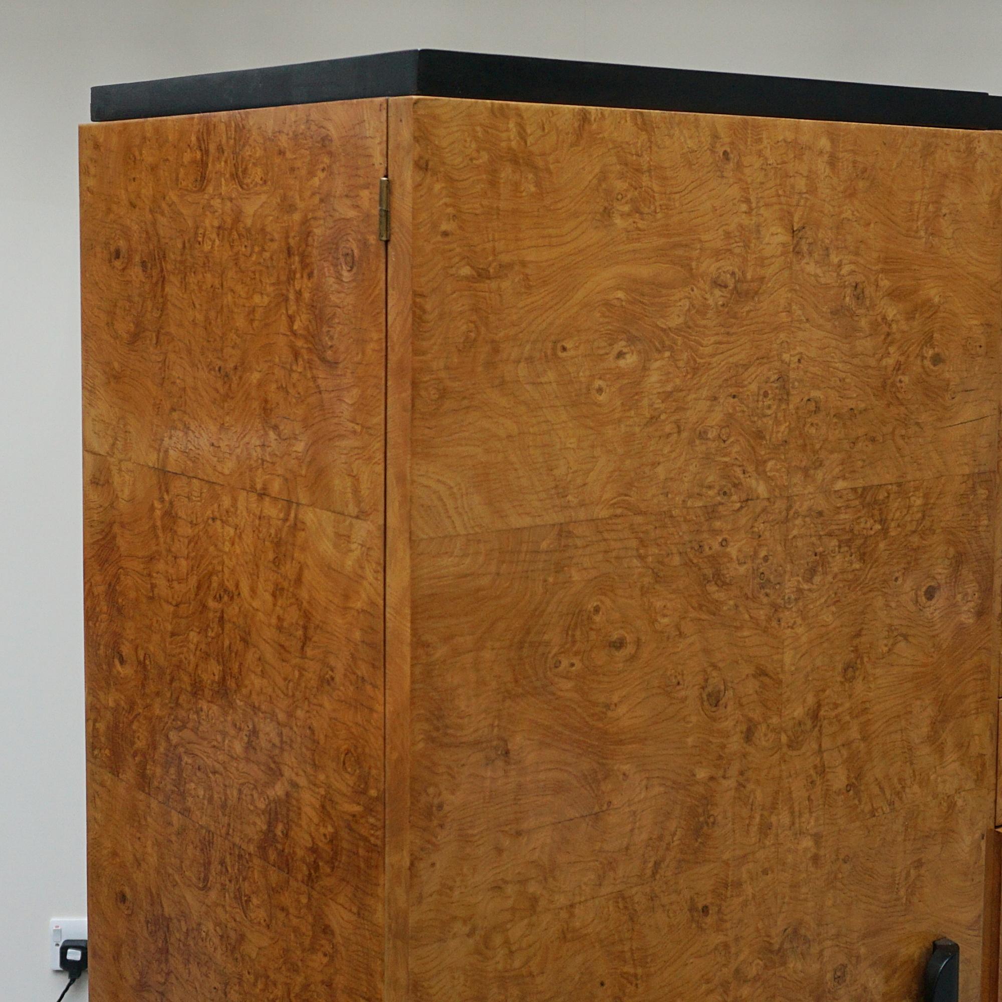 An Art Deco three sectioned dressing cupboard. Central variegated drawers flanked by to interior mirrored shelving compartments. Burr elm on solid mahogany with ebonised handles. Easy to dismantle and ship in parts.

