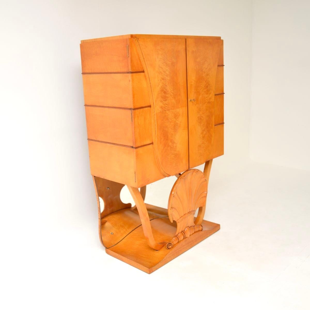 A stylish and exceptionally well made Art Deco burr walnut and sycamore cocktail cabinet by Hille, dating from the 1930’s.

This is of outstanding quality and has a gorgeous design. It stands on a stunning base with a large carved shell motif at the