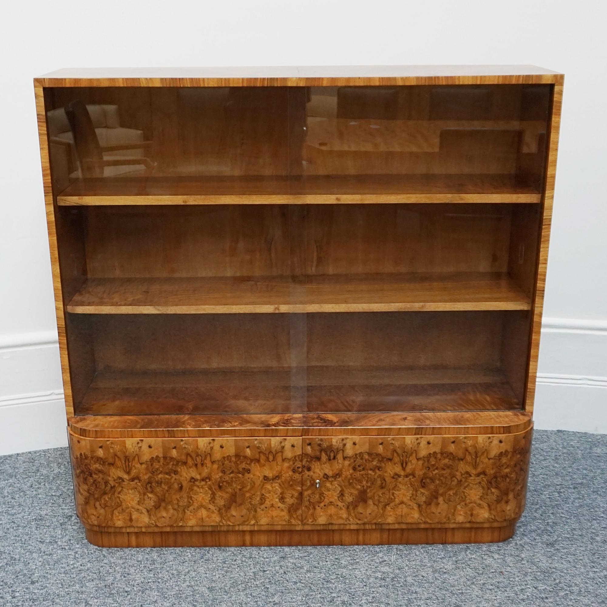 An Art Deco bookcase. Sliding glass doors with three interior adjustable solid walnut shelves and deep storage to lower section. Burr walnut veneered with figured walnut banding. 

Dimensions: H 78cm W 134cm D 63cm 

Origin: English

Date: Circa