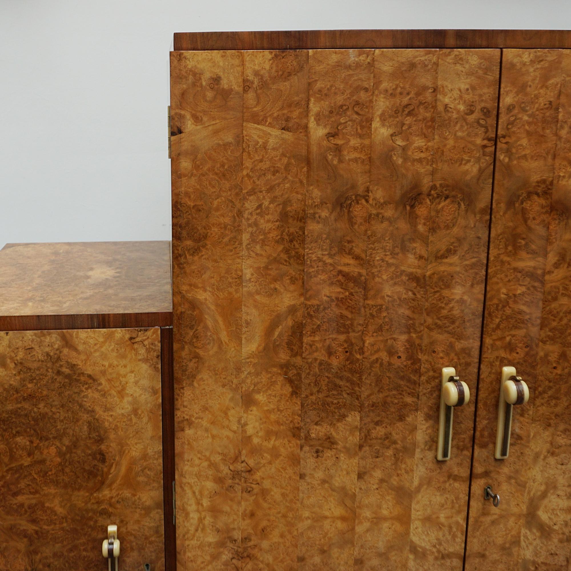 An Art Deco cocktail cabinet by Harry & Lou Epstein. Burr walnut veneered  with satin birch lined interior. Interior shelveing to either side with bottle storage to lower centre. Original peach mirrored glass interior with pull out sliding tray. Set