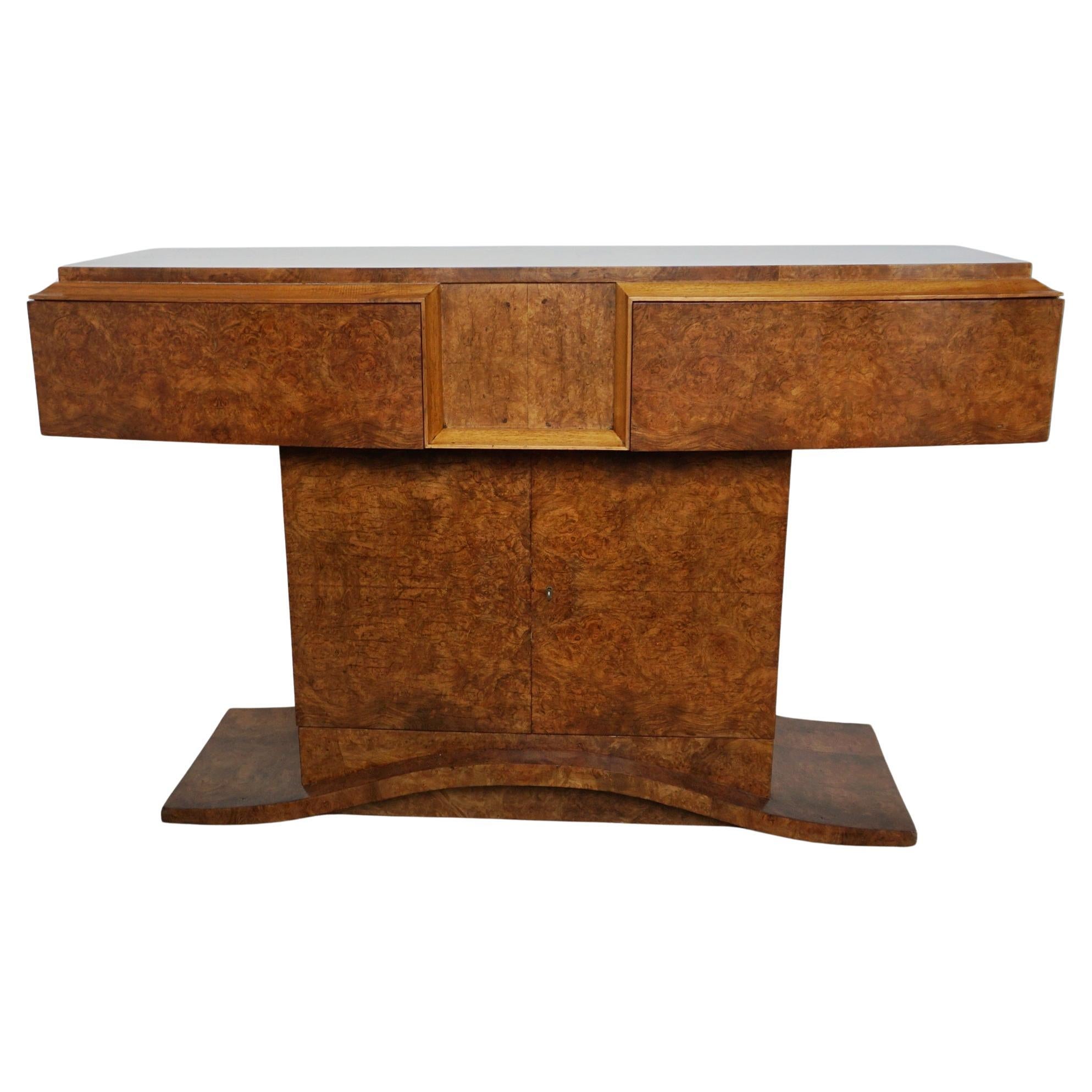 An Art Deco Console Table by Hille. Burr walnut veneered with figured walnut banding. Central opening cabinet with two pull out draws above set over a curved base. Glass protective top not photographed.

Dimensions: H 85cm W 135cm D 43cm

Origin: