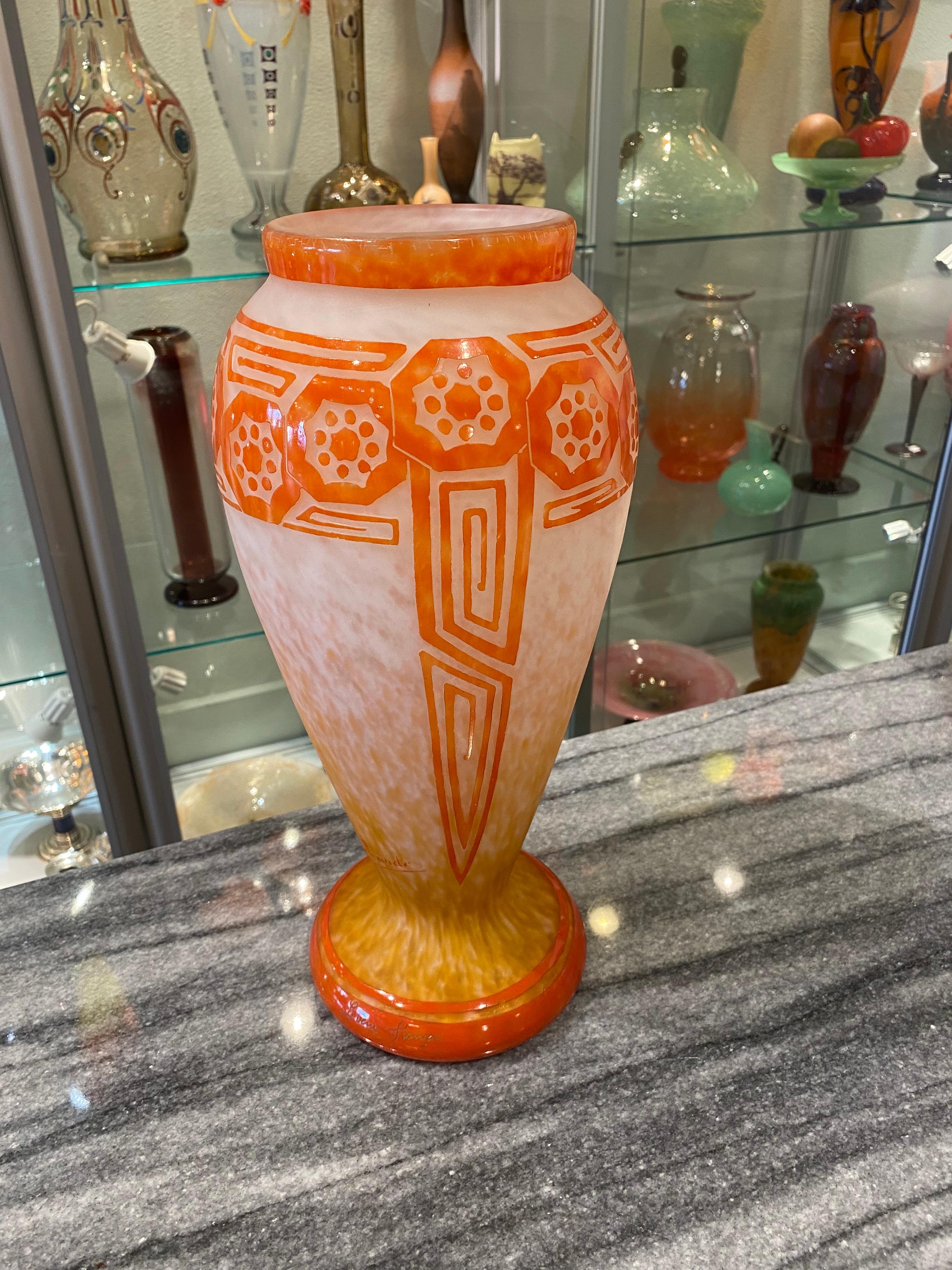 A glass vase from the Deco serie of Le Verre Français.  This vase has a White Opalescent background with degradé of Orange.  The foot and motif (flowers and geometric pattern) on this vase are in a darker Orange. The patter is