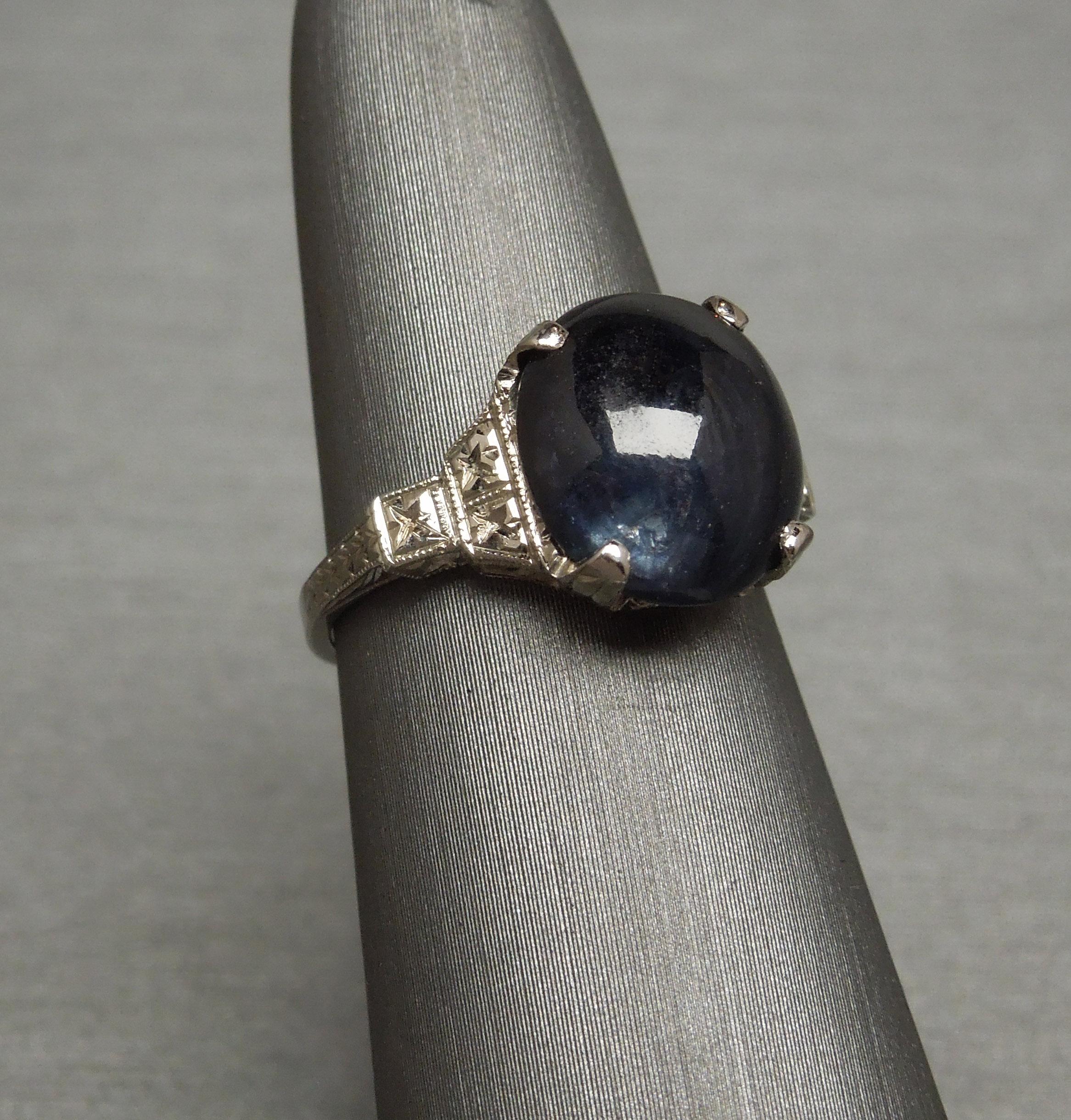 This period Art Deco Sapphire Solitaire ring in 14KT White Gold is subtly accented with exceptionally detailed Hand Engraving from prong tips to about 6.2mm down each side of band as well as some Milgrain detailing. Featuring a lone 6.85 carat Oval