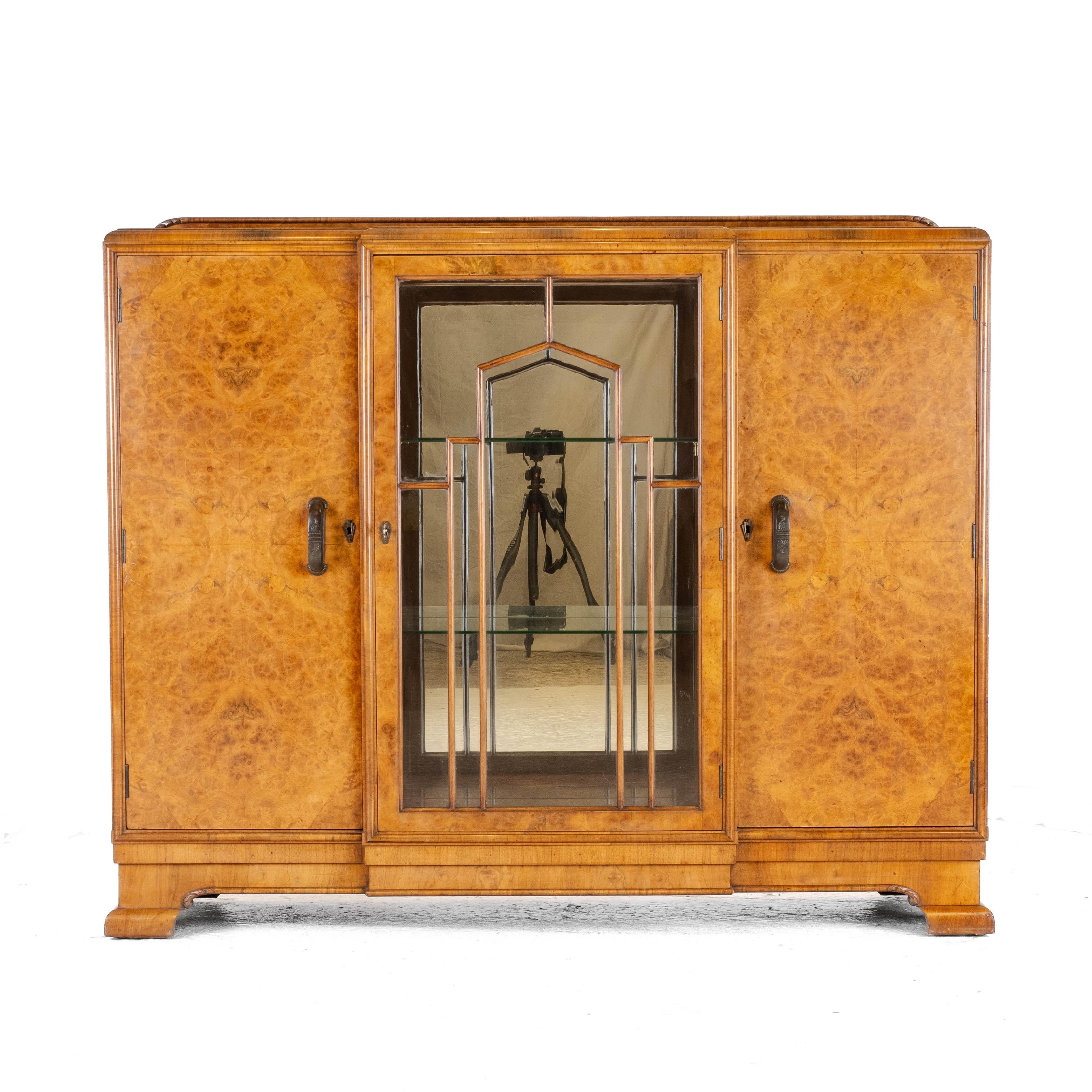 An Art Deco period, circa 1920, burr walnut display cabinet / sideboard, by Leemings of Halifax, England. This handsome triple cabinet sideboard features beautifully figured burr walnut throughout. The oblong shaped top with shaped back stand, and