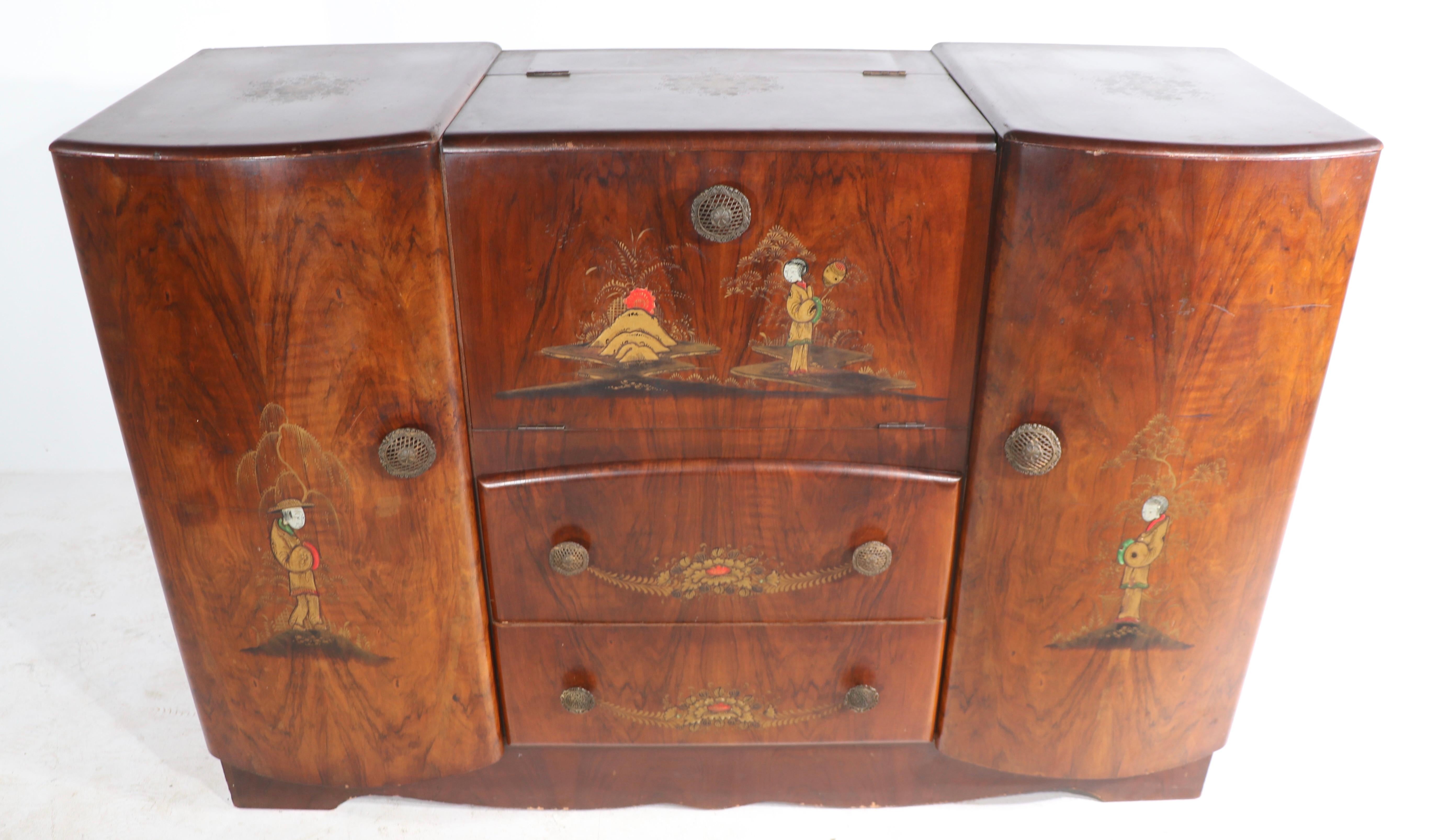 English Art Deco cabinet dry bar, having a mirrored interior, and hand painted Japanese figures etc on the case.
The middle section opens to reveal a work surface and storage for your barrage, mixing tools, glasses etc. The two side doors and