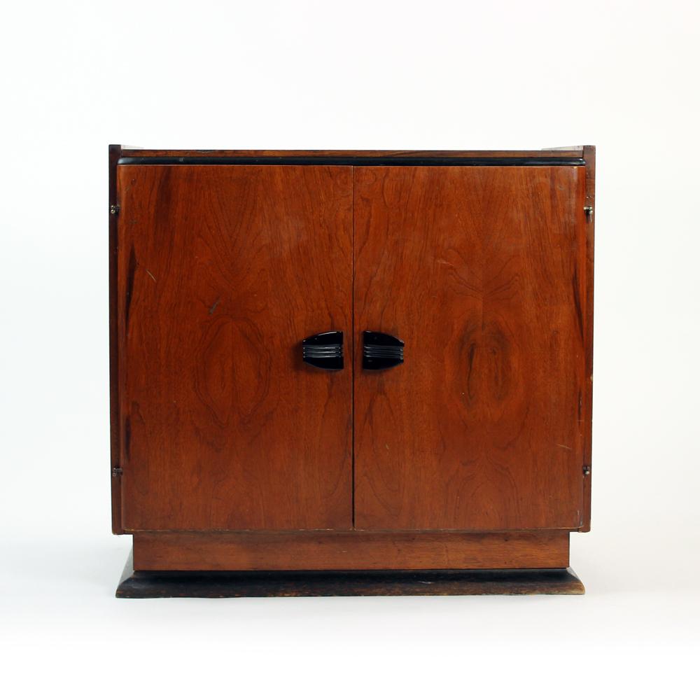 This is a very elegant cabinet from Art Deco era. Made of wood with mahogany veneer and black wooden details on bottom and top. Very elegant sheen on the wood. Inside the cabinet has one shelf and a book separating sliding wood piece on a metal